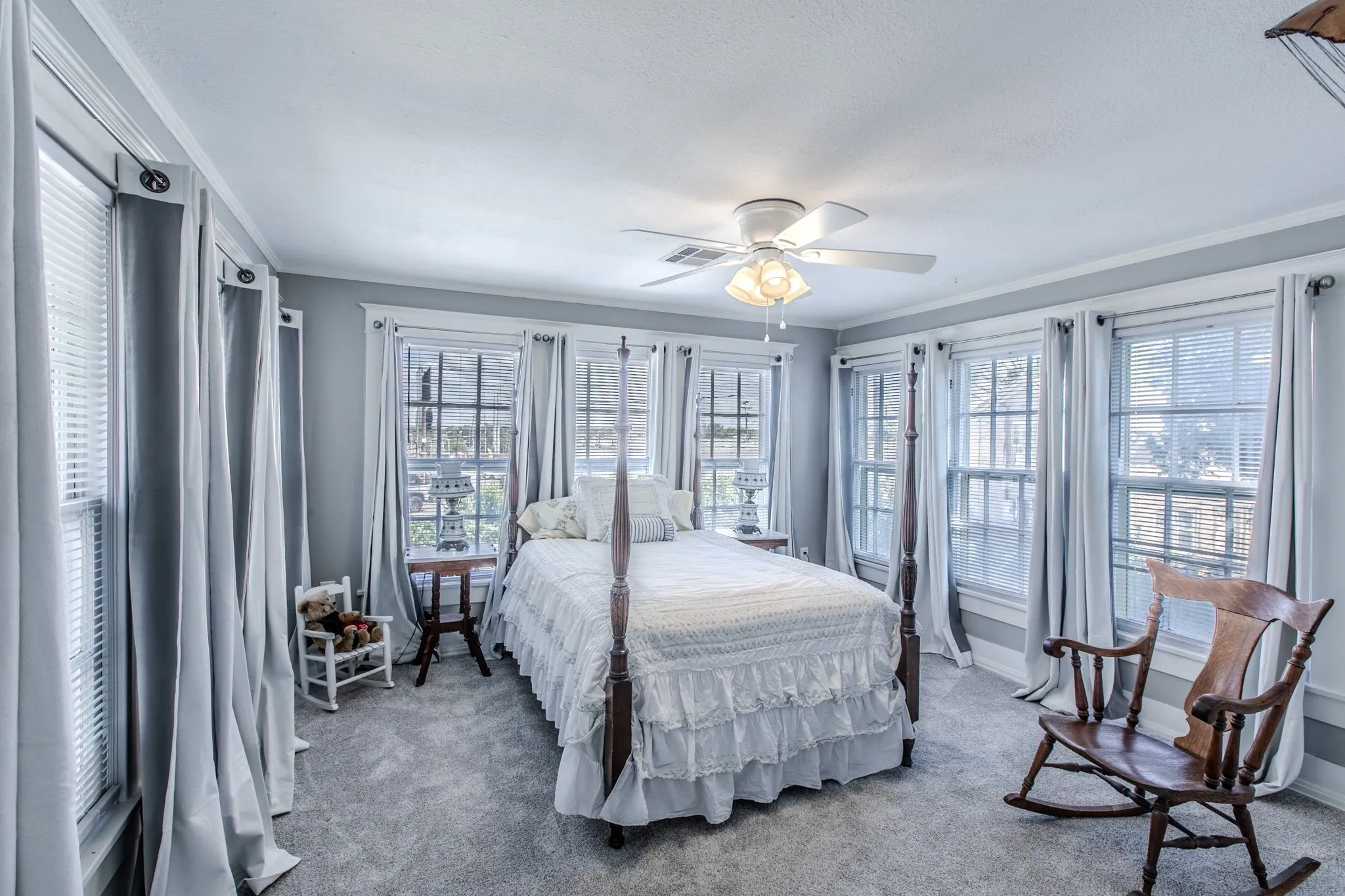 Neutral-toned wall paint, multiple windows with blinds, ceiling fan with integrated lighting, and carpeted flooring
