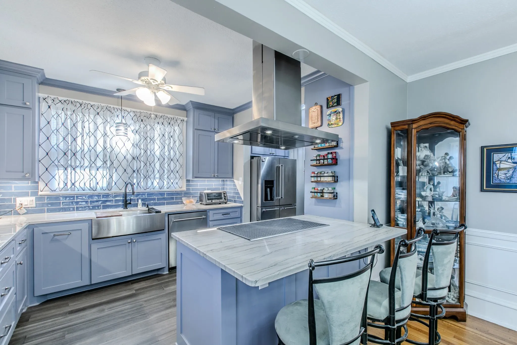 Kitchen featuring light blue cabinetry, stainless steel appliances, a center island with integrated cooktop, a stainless steel farmhouse sink, and wood-finish flooring