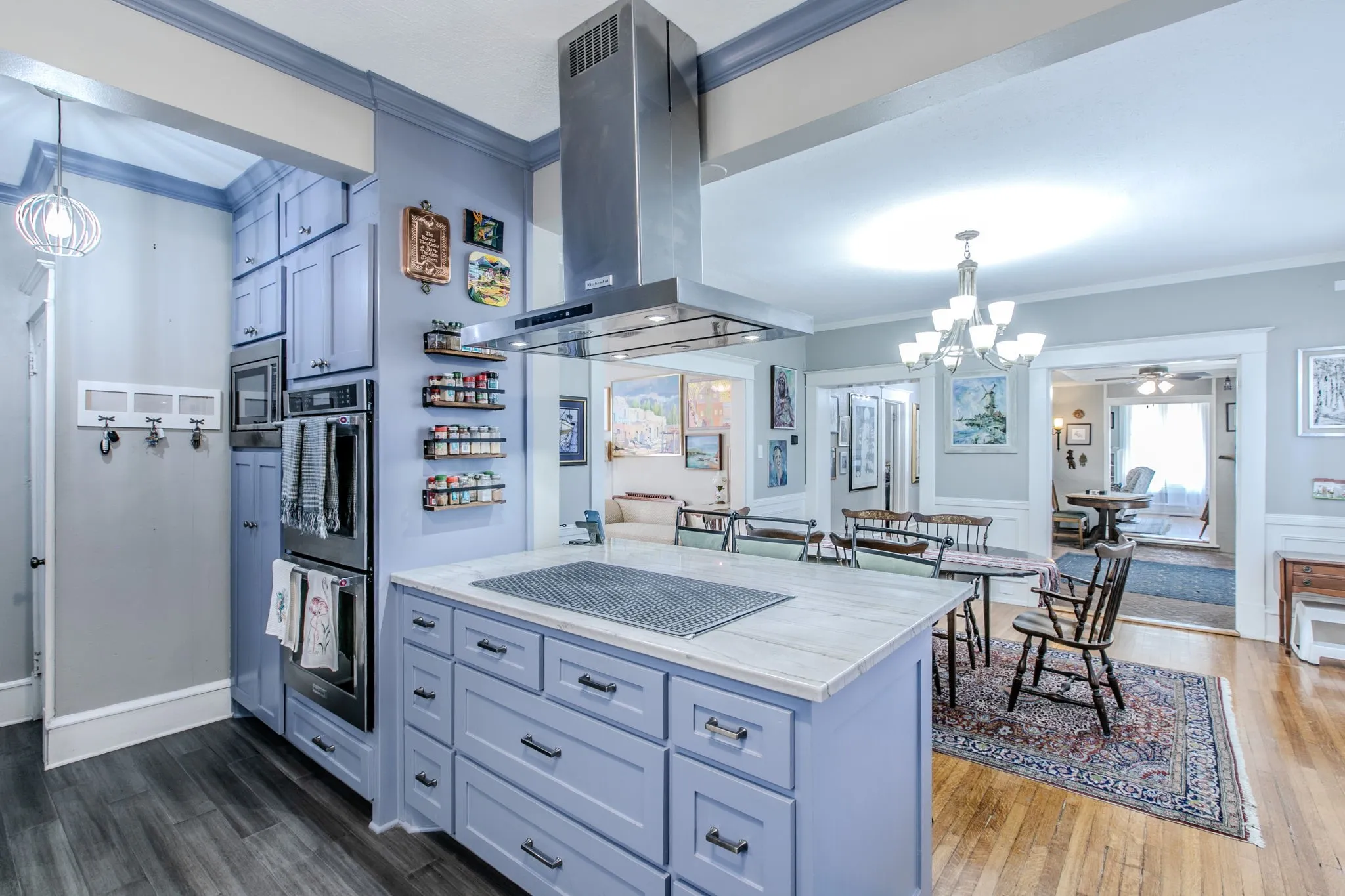 Kitchen featuring light blue cabinetry, built-in double ovens, a stainless steel range hood, and an island with a light-colored countertop