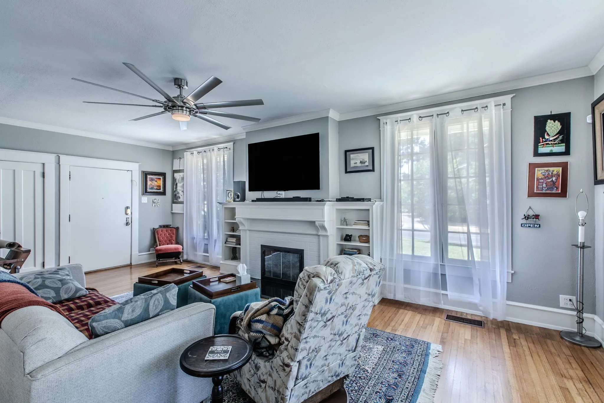 Hardwood flooring, crown molding, built-in fireplace with mantel, ceiling fan, and large windows
