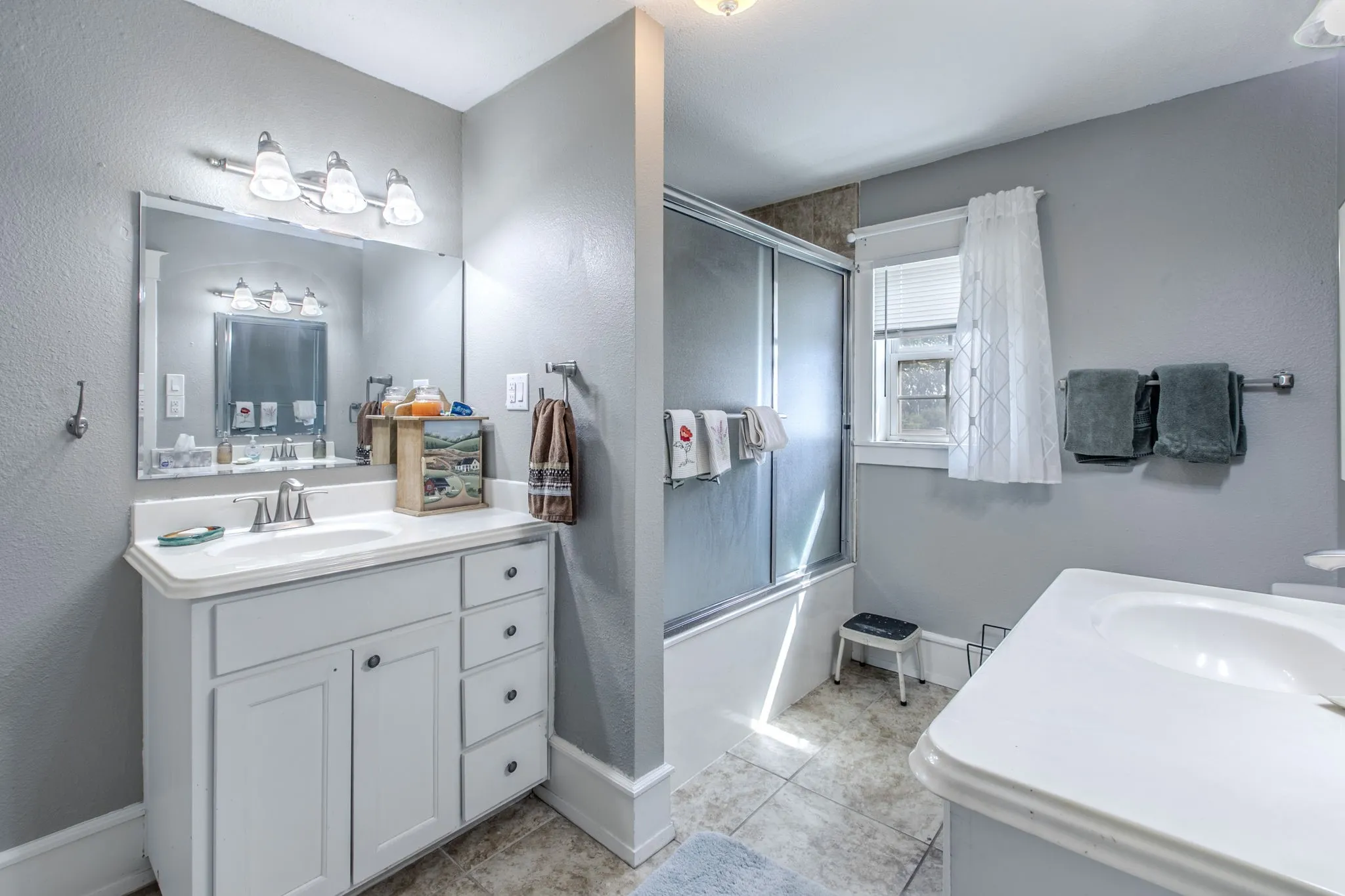 Spa-inspired primary bathroom featuring a white vanity with ample storage, dual-sink configuration with chrome fixtures, framed mirror with integrated lighting, tile flooring, soaking tub, and a walk-in shower with glass enclosure and white subway tile surround