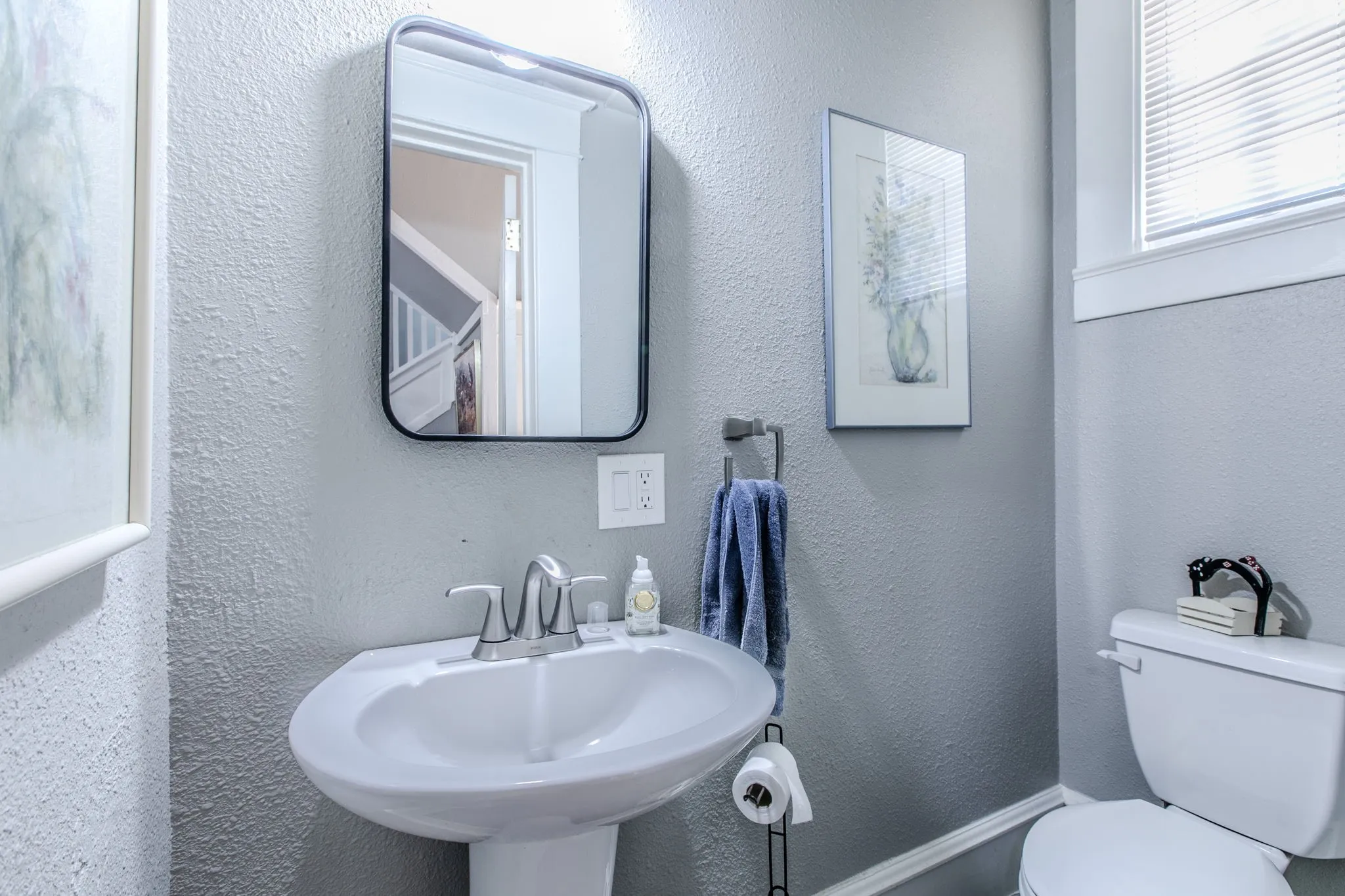 Pedestal sink with chrome faucet, framed mirror, and a window with blinds