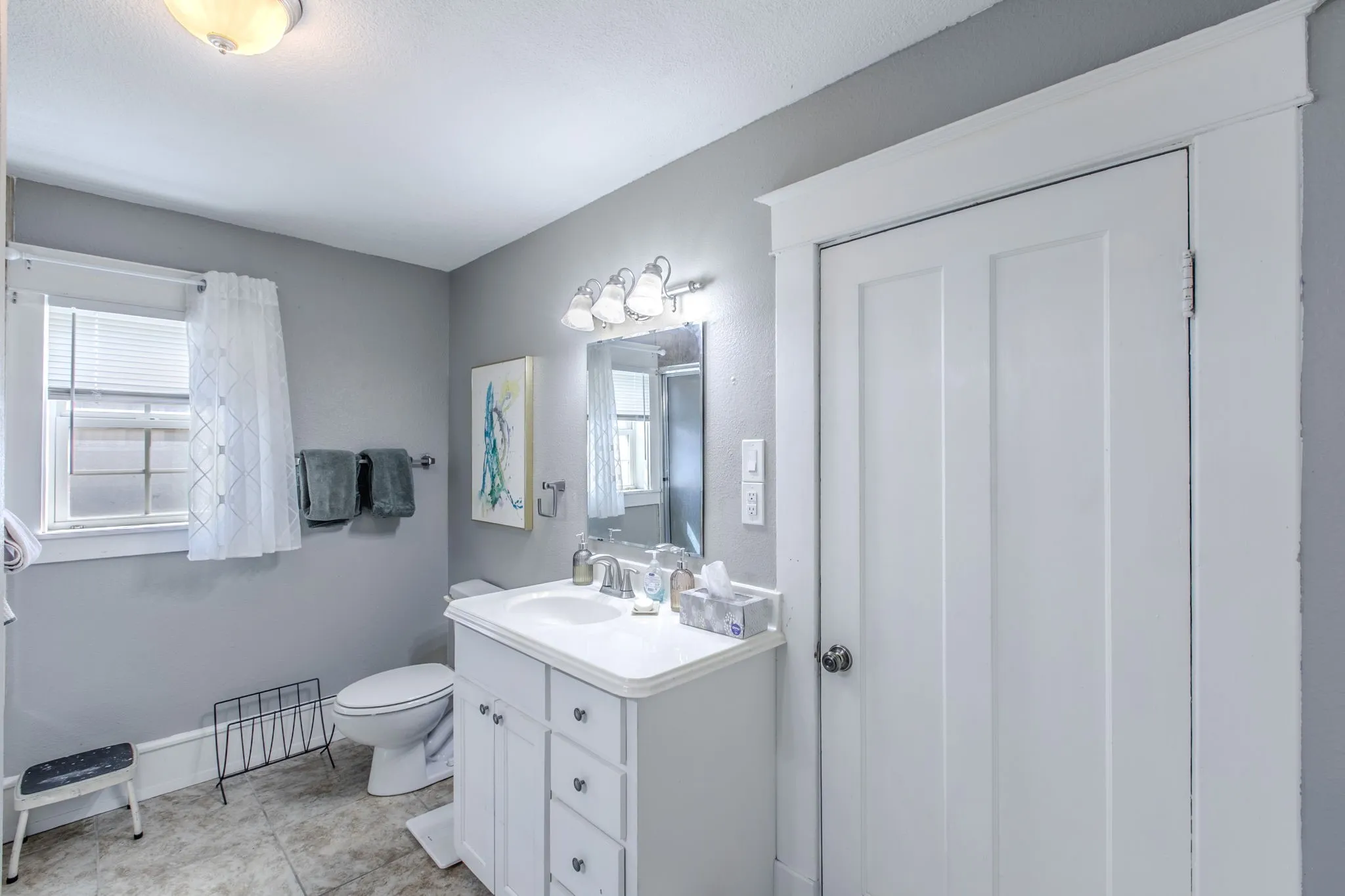 White panel door with detailed trim, white vanity with integrated sink, chrome-finish fixtures, and a wall-mounted light bar