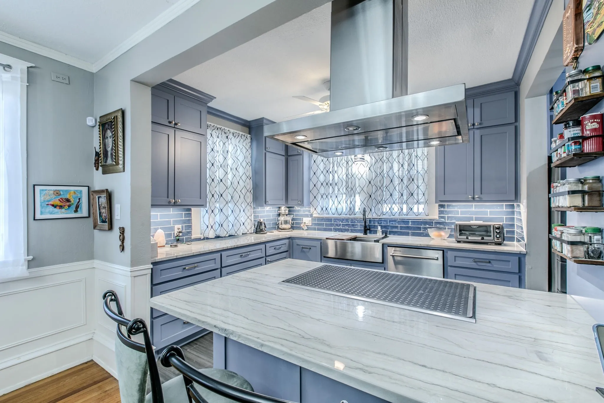 Spacious kitchen featuring an expansive central island, stainless steel range hood, ample blue cabinetry, subway tile backsplash, and a large stainless steel sink