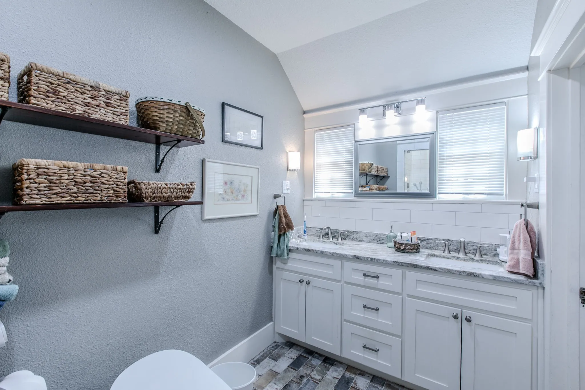 Double vanity with integrated sinks, granite countertop, subway tile backsplash, and two wall-mounted sconces