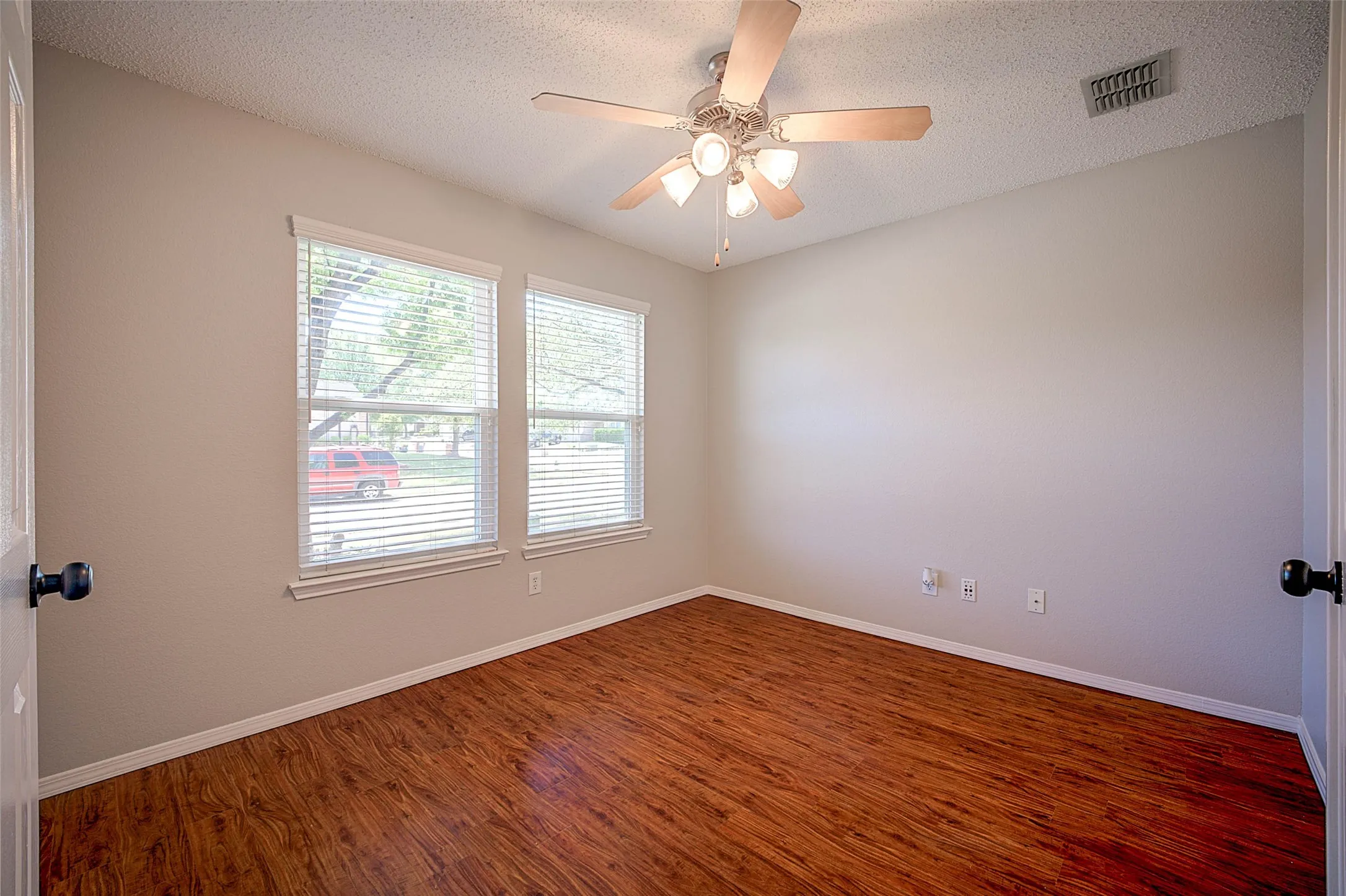 Wood-finish flooring, two windows with blinds, ceiling fan with integrated lighting, and neutral wall tones