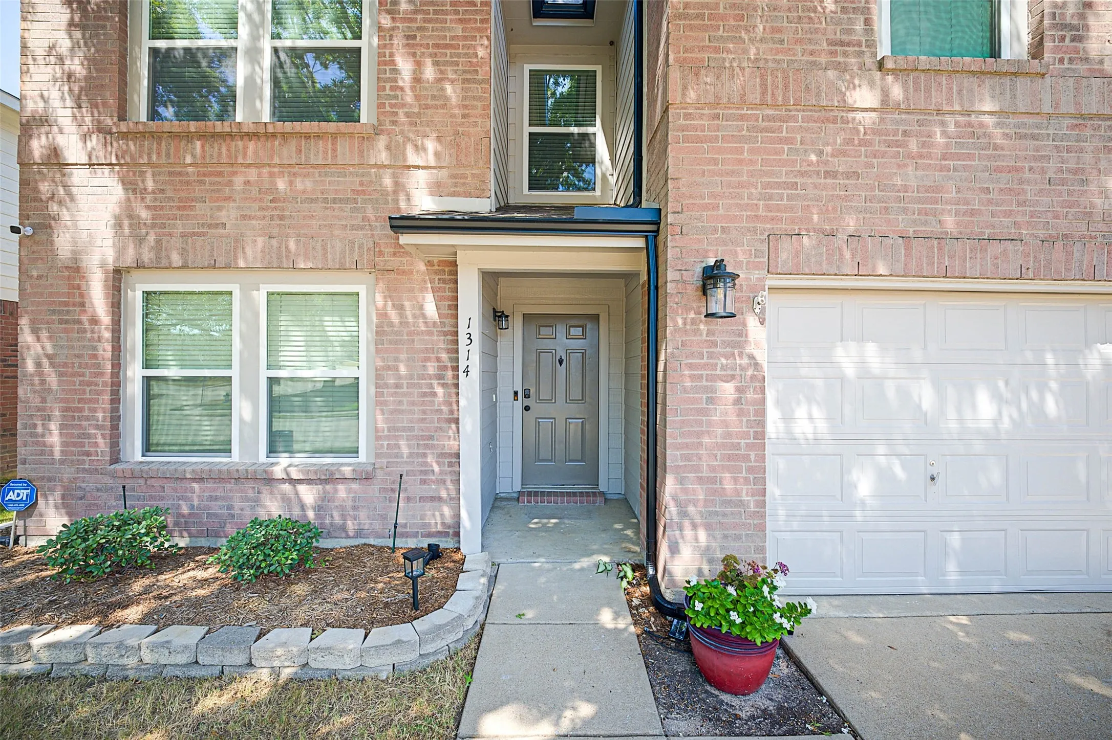 Brick exterior, white-framed windows, white garage door, covered entry, and a landscaped planting bed