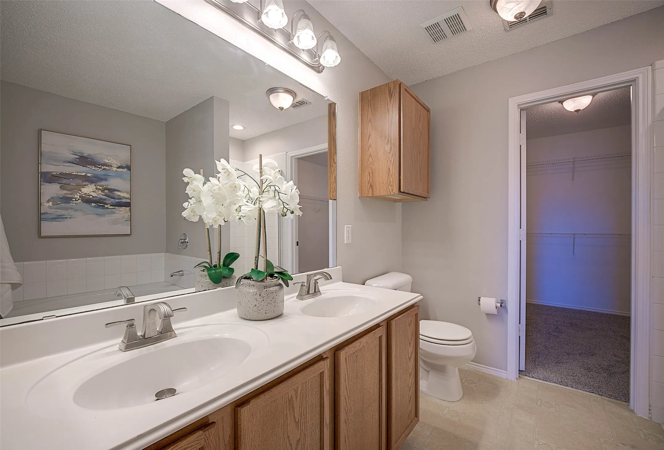 Dual vanity with integrated sinks, wood-finish cabinetry, a large mirror, and overhead lighting