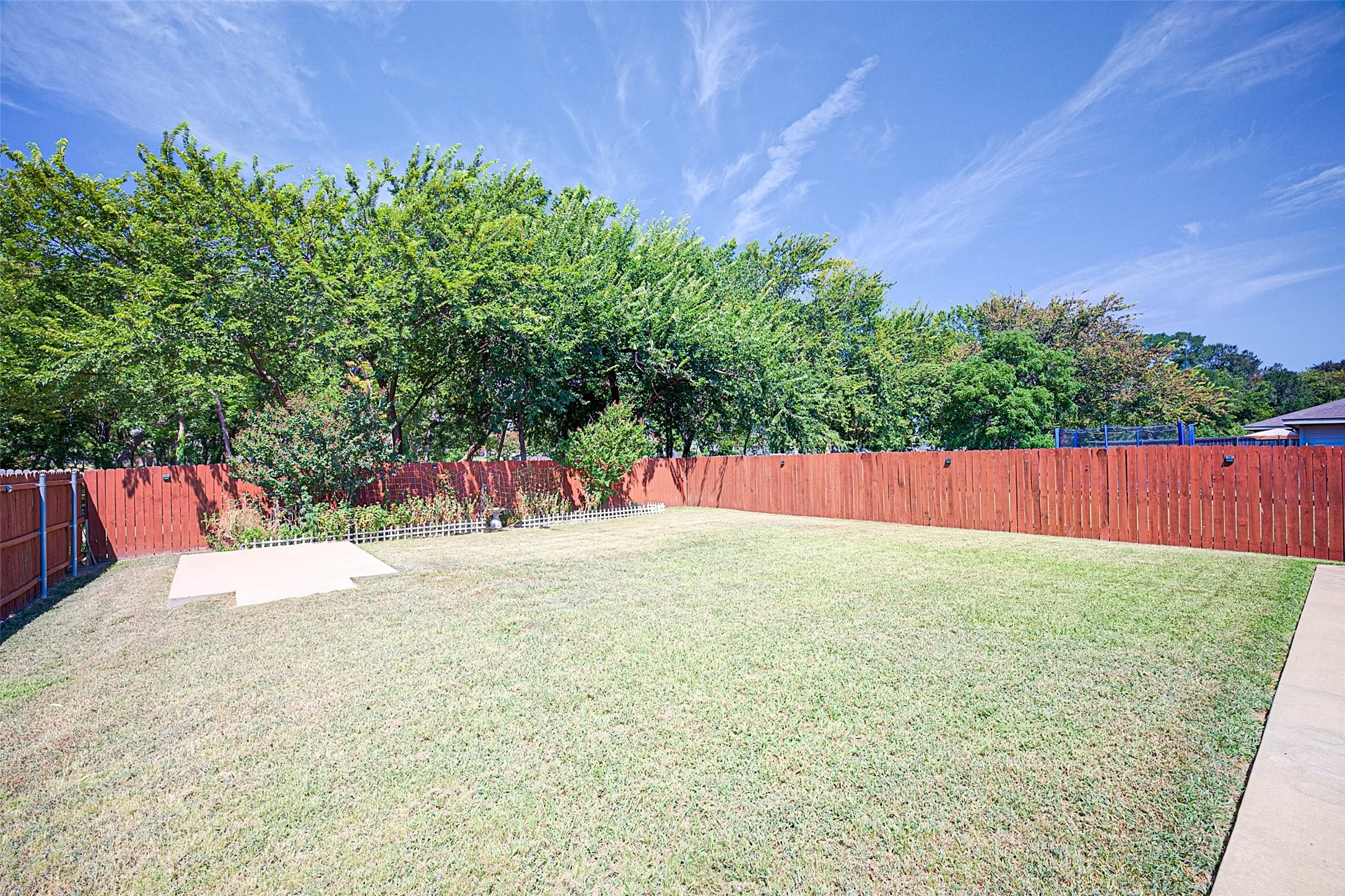 Expansive grass lawn with a perimeter wood fence, mature trees, and a concrete patio pad