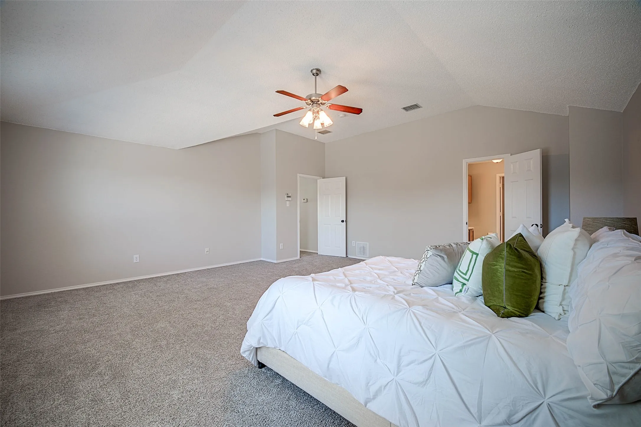 Vaulted ceiling with a wood-finish ceiling fan, neutral wall tones, and plush carpeting