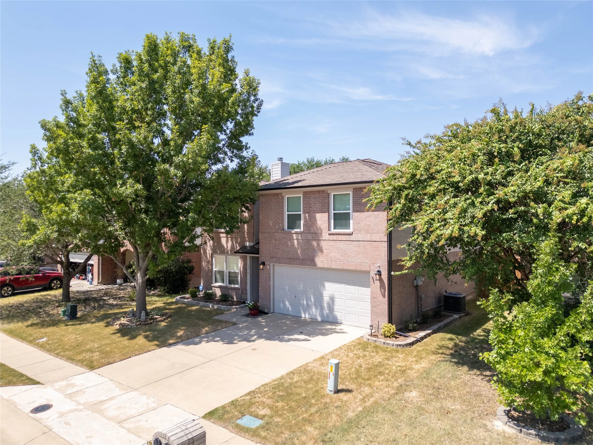 Brick exterior with a two-car garage, mature trees, and a concrete driveway