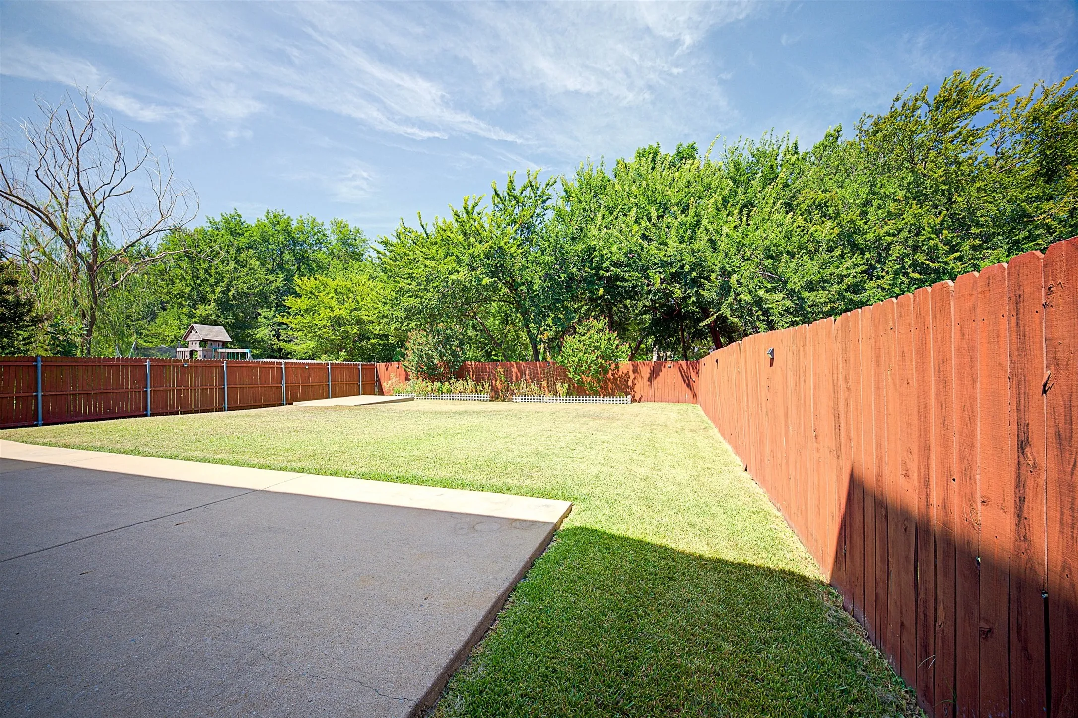 Expansive grassy yard with mature perimeter trees, wood privacy fencing, and a concrete patio