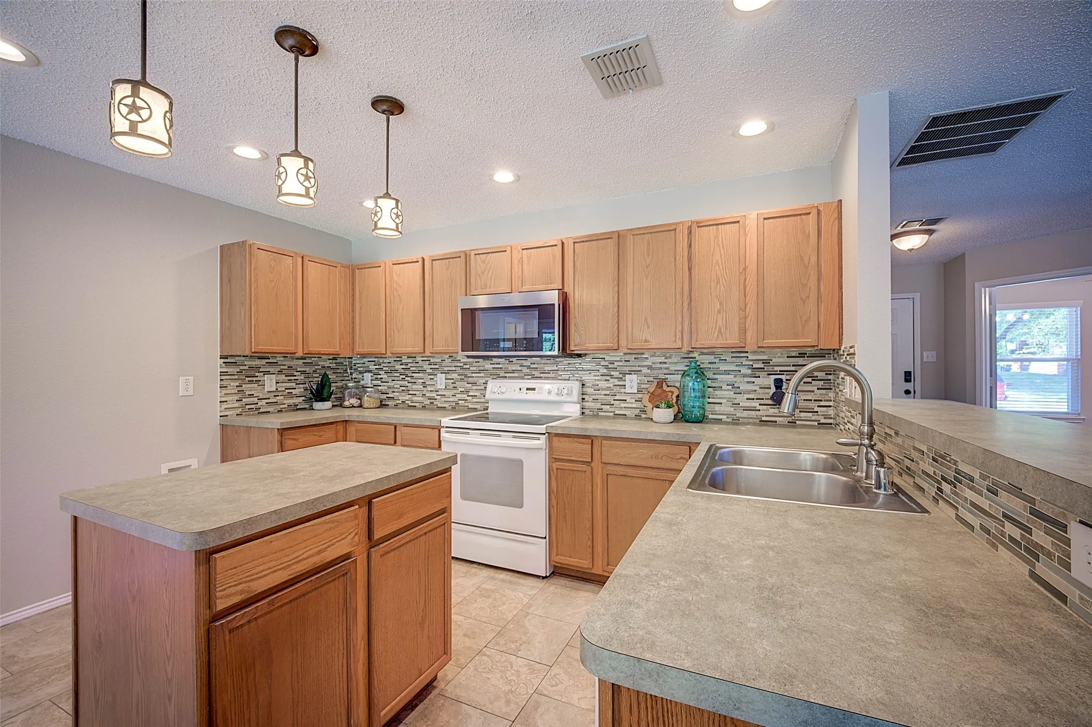 Kitchen featuring wood-finish cabinetry, a central island, mosaic tile backsplash, recessed lighting, and a stainless steel double-basin sink