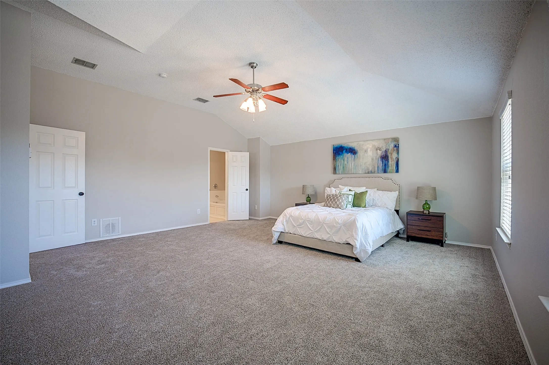 Spacious interior featuring vaulted ceilings, ceiling fan, neutral carpet, and a large window with blinds