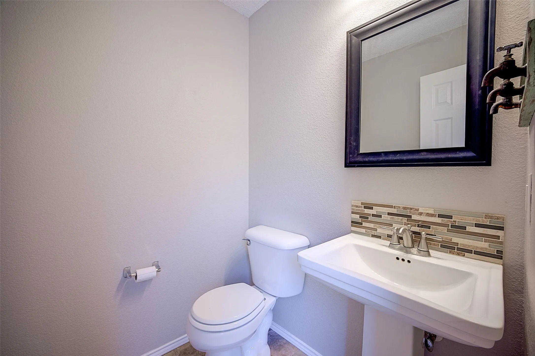 Pedestal sink with mosaic tile backsplash, framed mirror, and chrome fixtures