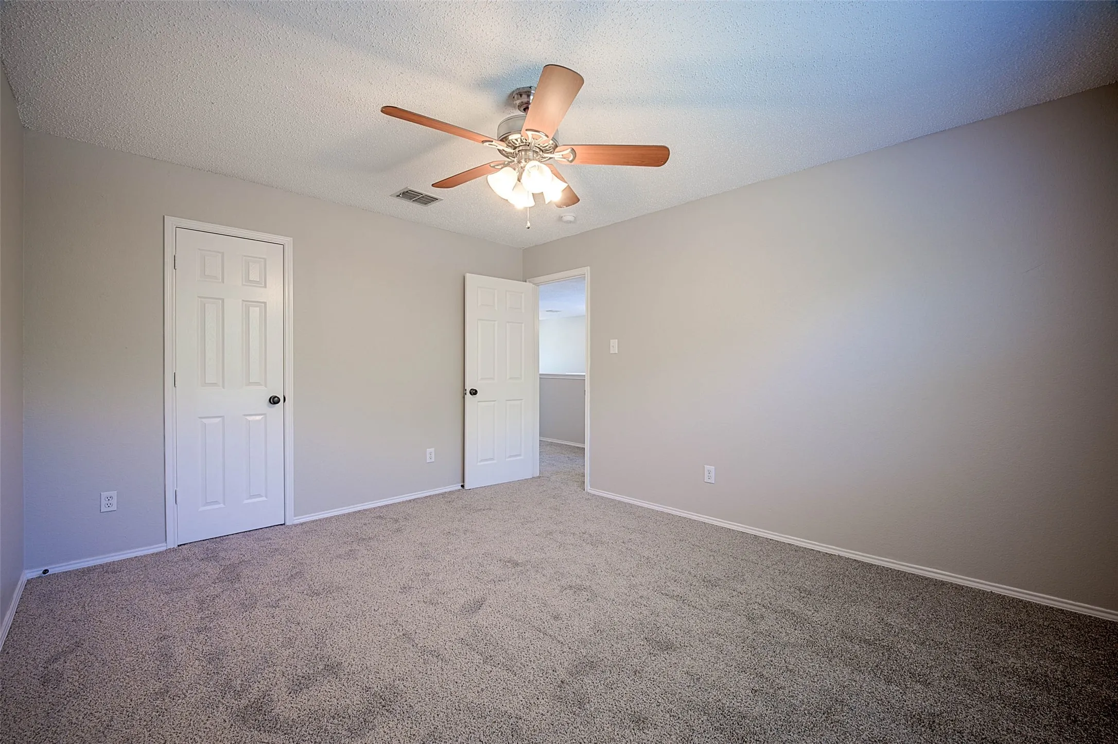 Neutral tone wall paint, textured ceiling, ceiling fan with integrated lighting, paneled interior doors, and carpet flooring