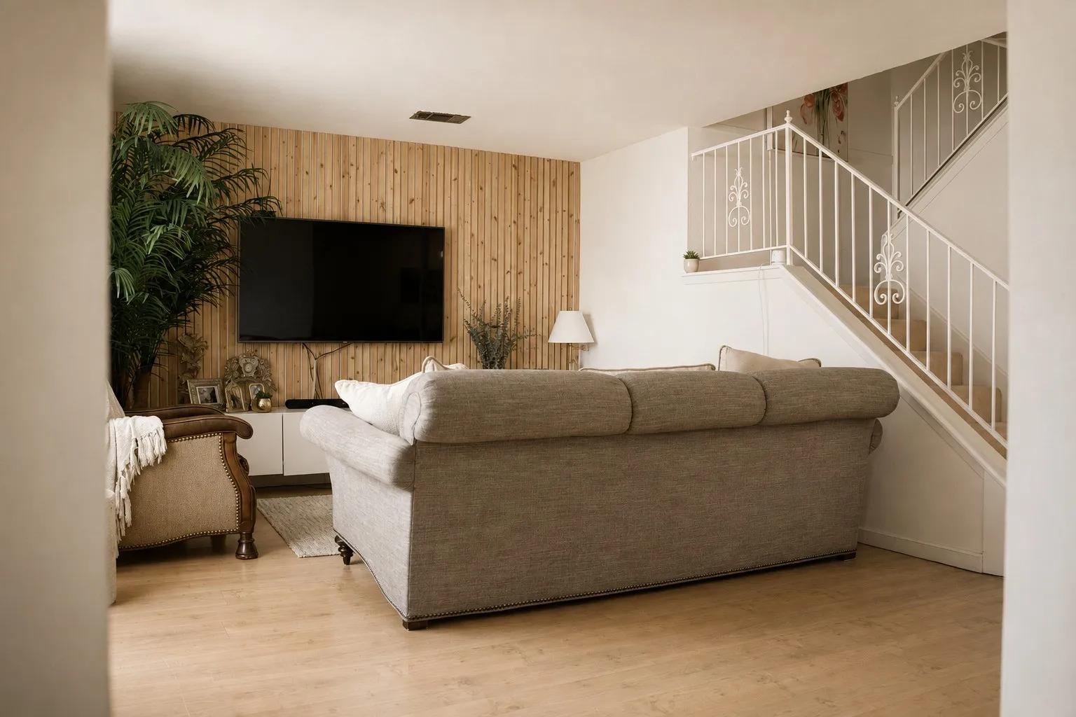 Wood-finish flooring, wood-paneled accent wall, white staircase with decorative wrought iron railing