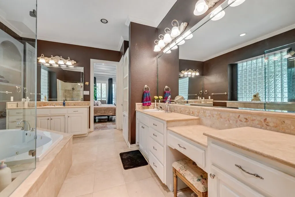 Dual vanities with light-colored countertops, a built-in jetted tub with a glass enclosure, light-colored tile flooring.