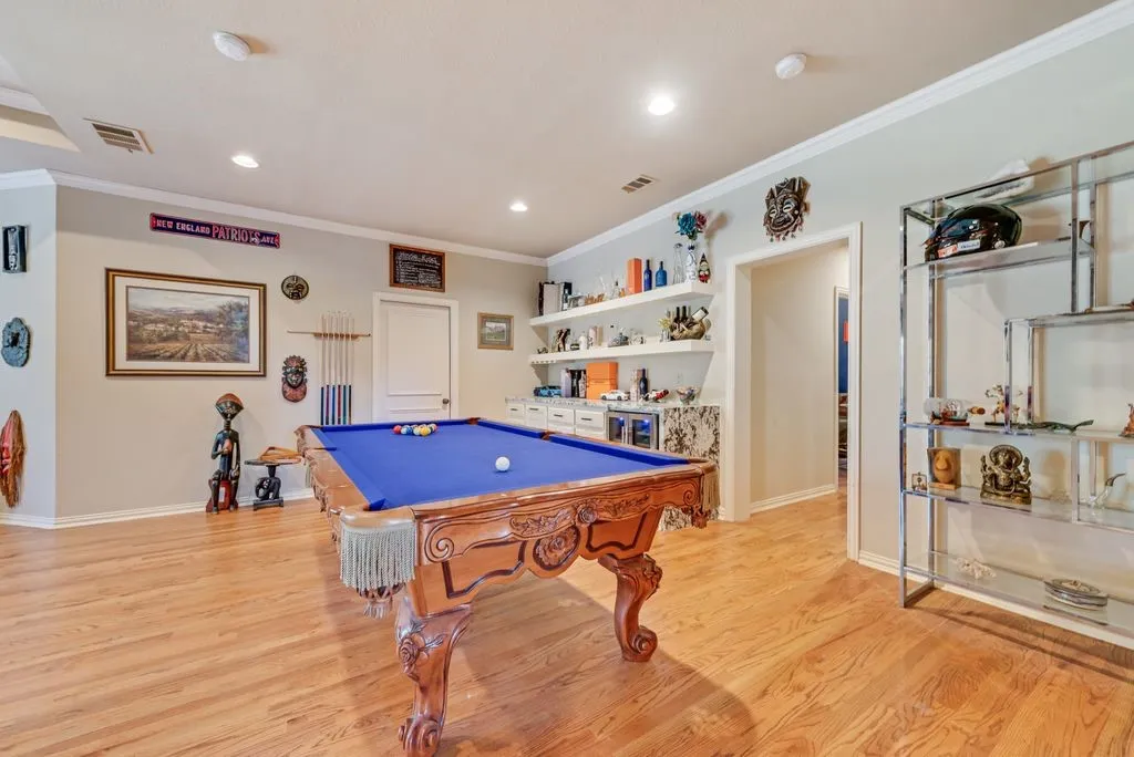 Hardwood-finish flooring extending throughout, featuring recessed lighting, crown molding, and a built-in bar with open shelving.