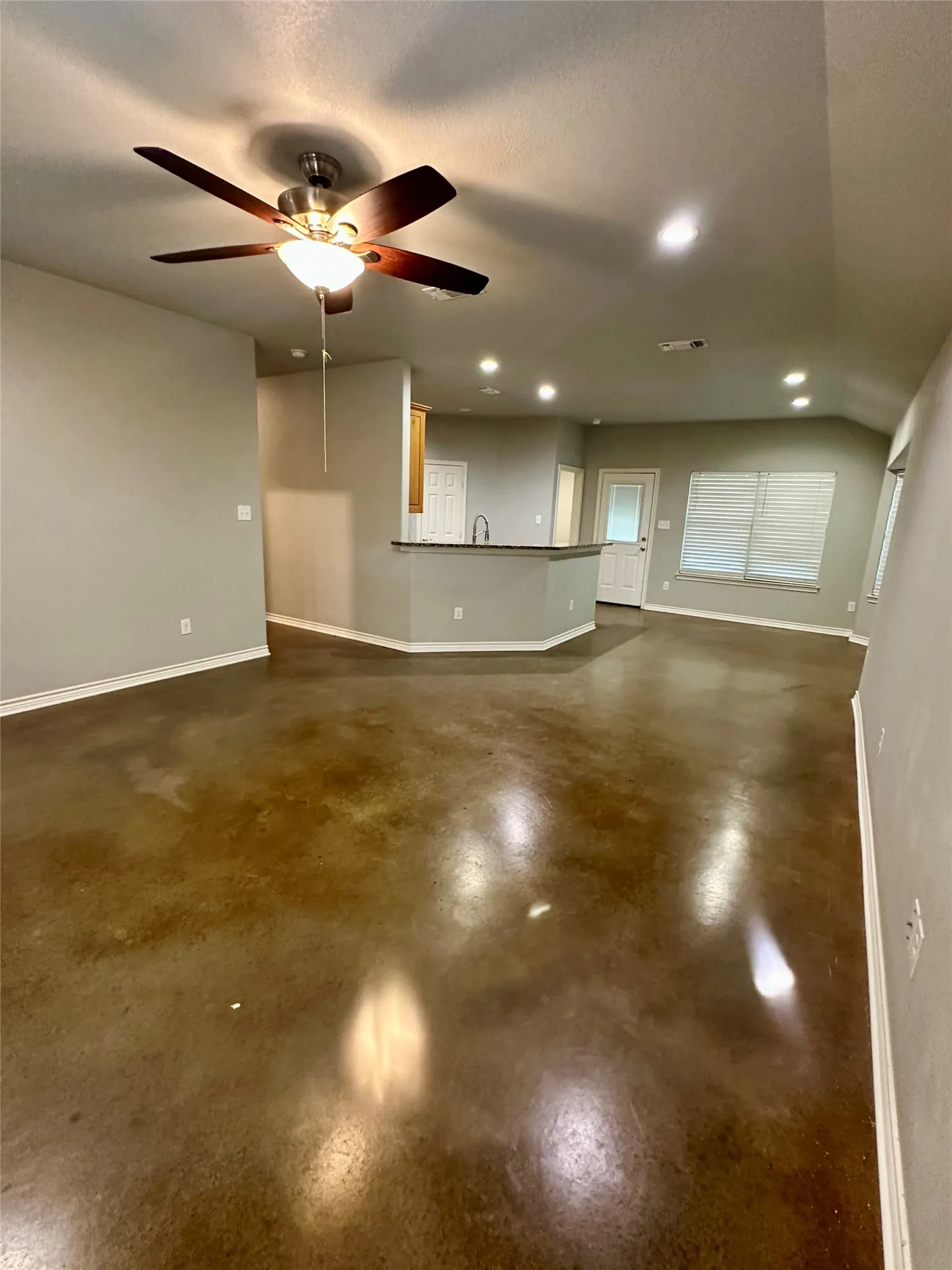 Living room featuring finished concrete flooring, baseboards, ceiling fan, recessed lighting, and a sink