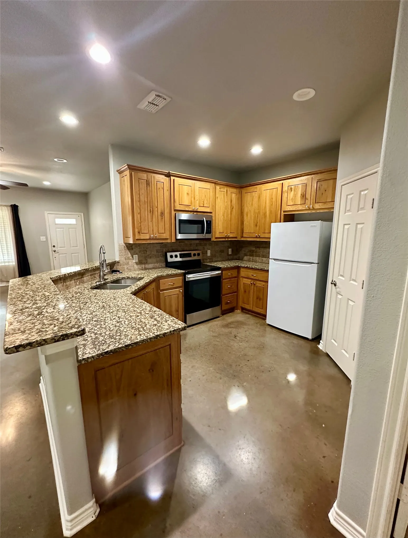 Kitchen featuring stainless steel appliances, a sink, a peninsula, tasteful backsplash, and dark stone countertops
