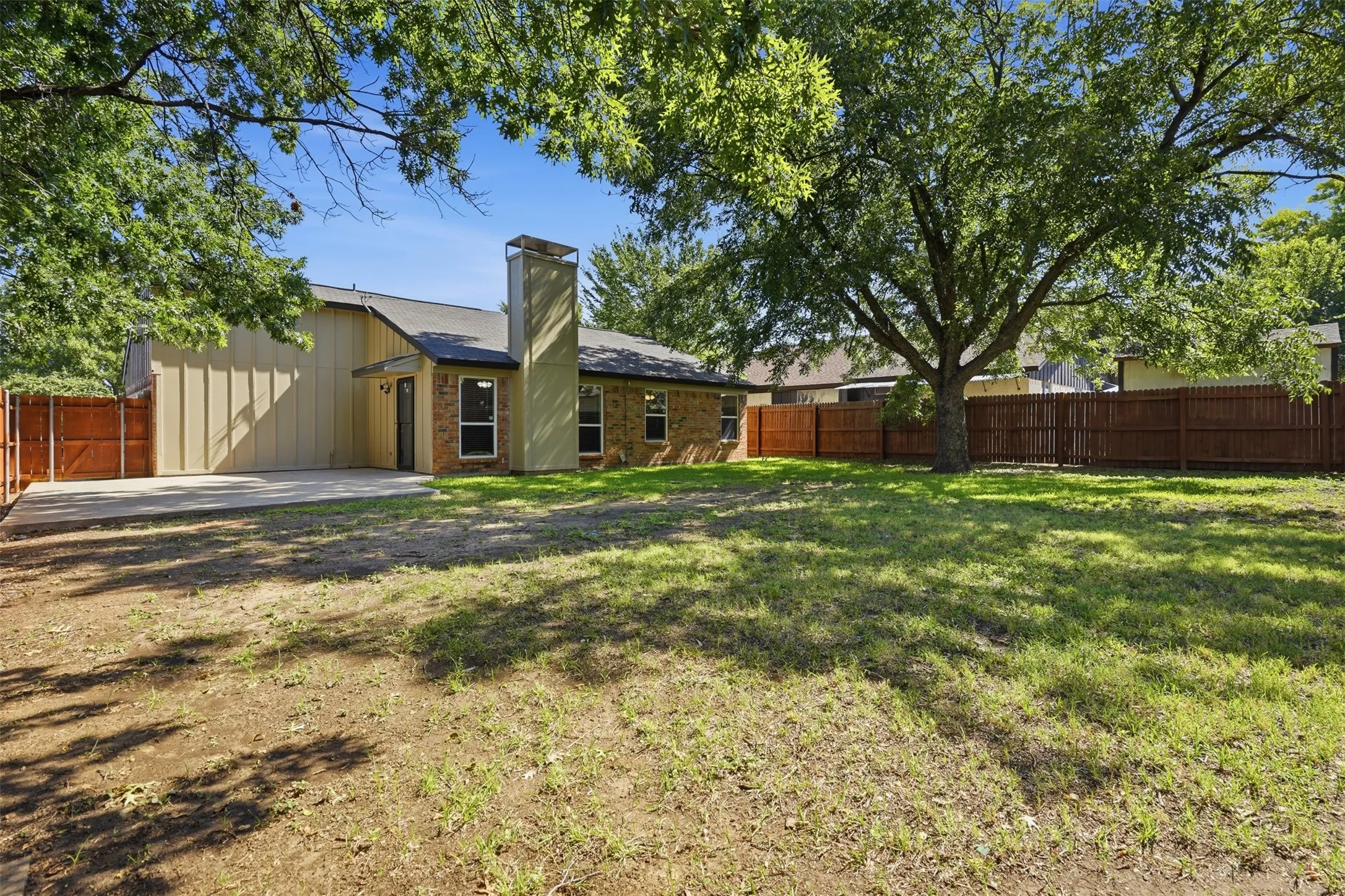 Expansive backyard featuring a mature shade tree, a concrete patio, and a wood privacy fence