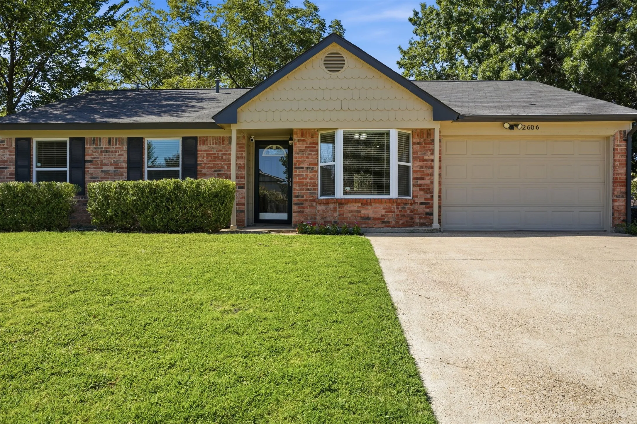 Brick facade with shuttered windows, a prominent garage, a bay window, and a concrete driveway