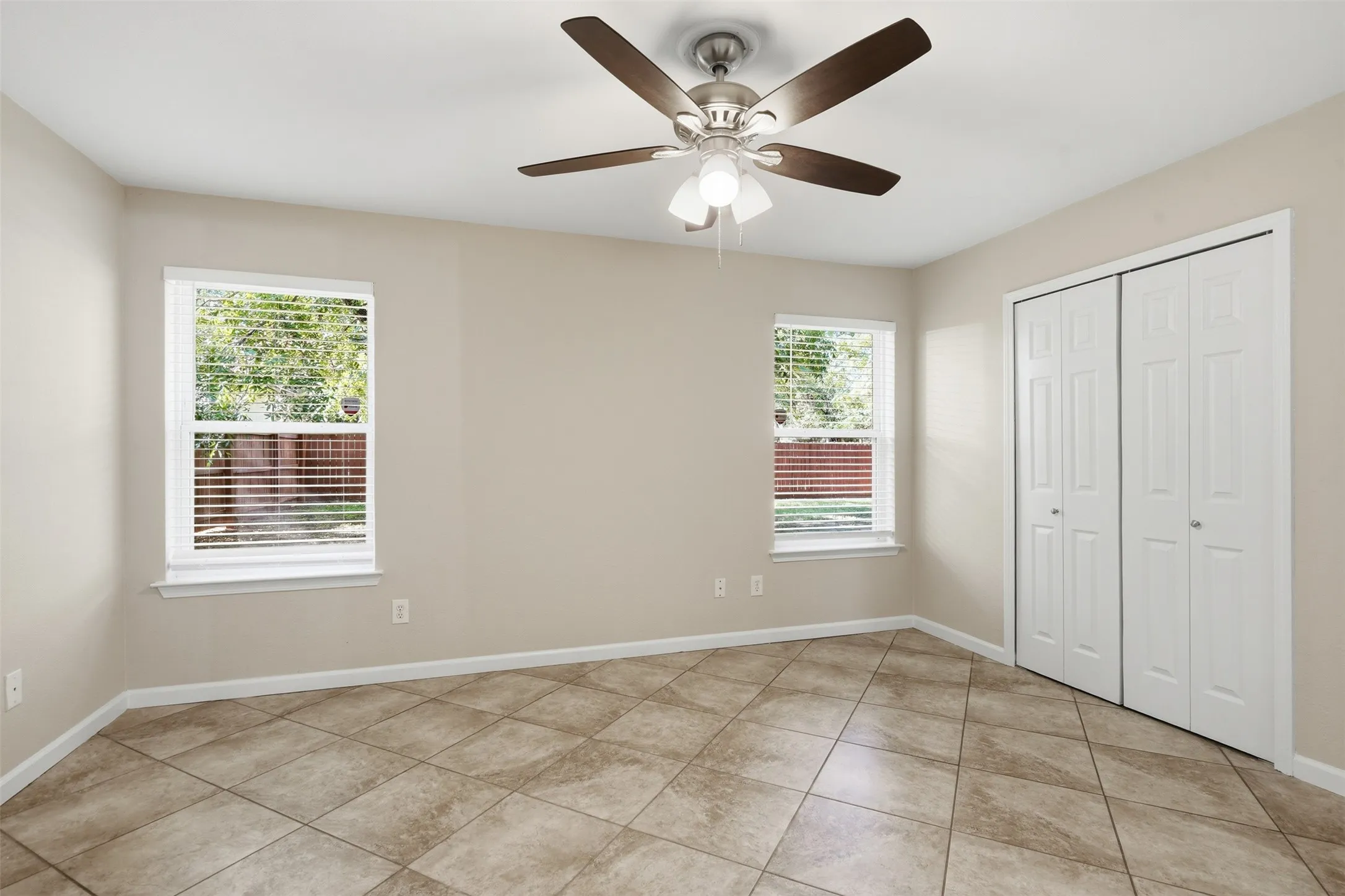 Tile flooring, ceiling fan with integrated lighting, two windows with blinds, and white bi-fold closet doors