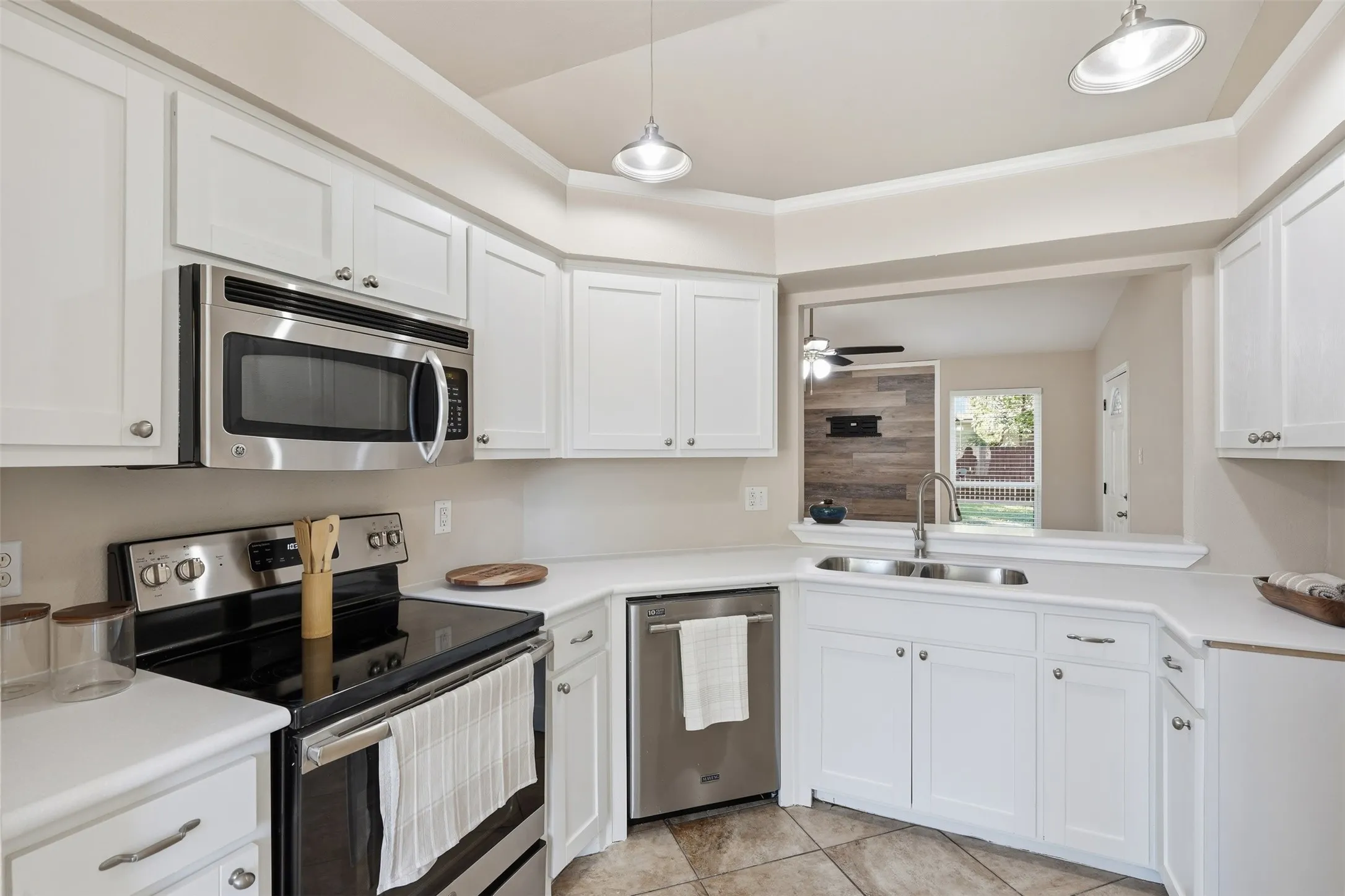 White cabinetry with brushed nickel hardware, stainless steel appliances, corner-set electric range, and solid surface countertops