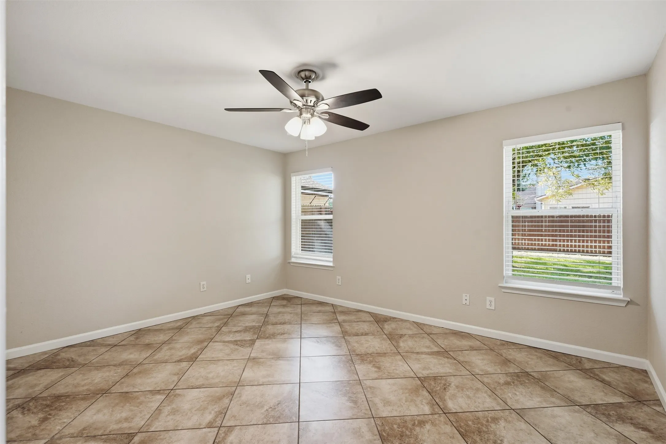 Neutral wall tones, tiled flooring, two windows with blinds, and a ceiling fan with integrated lighting