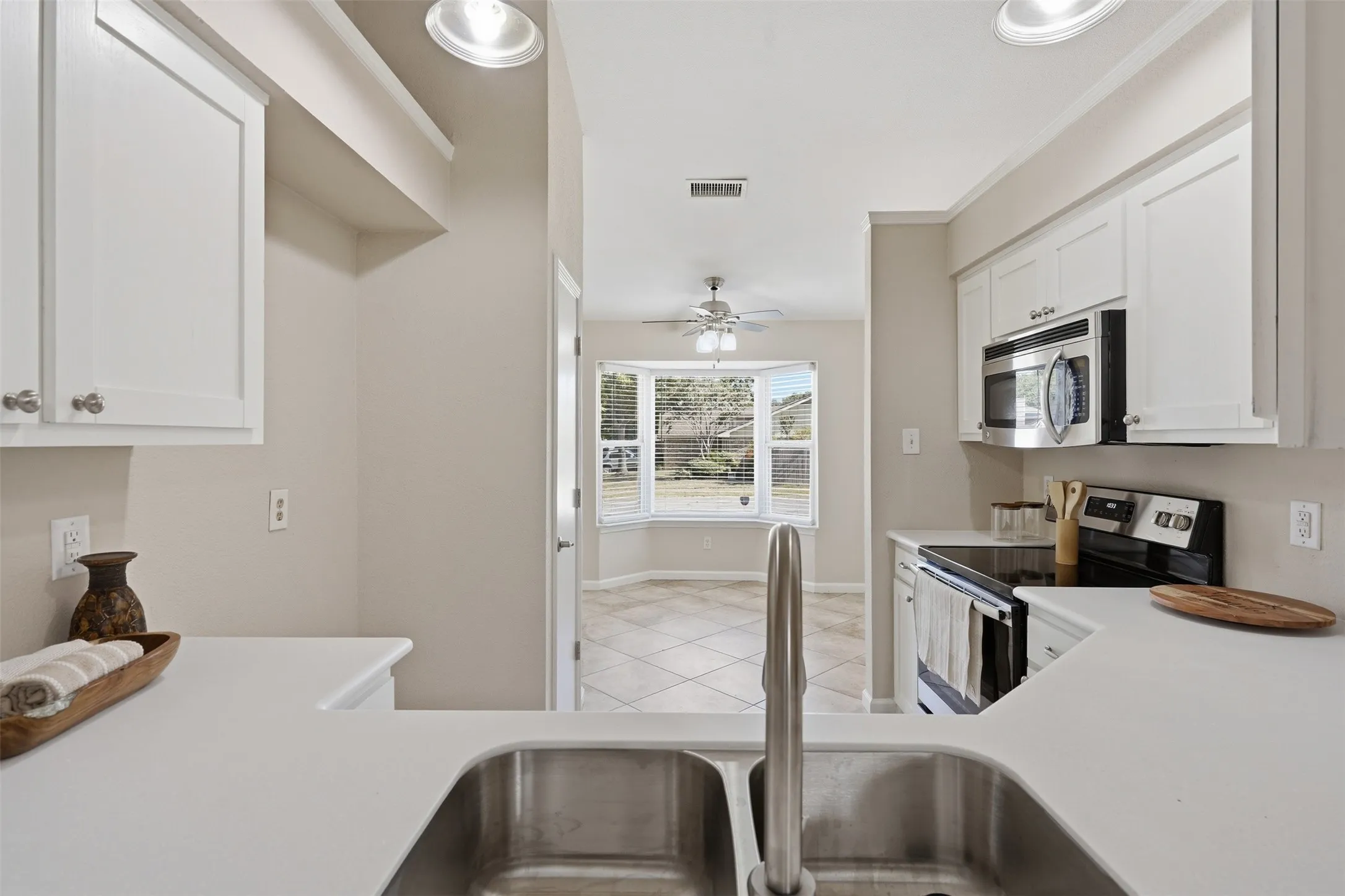 Kitchen featuring white cabinetry, stainless steel appliances, a double basin sink, and solid surface countertops