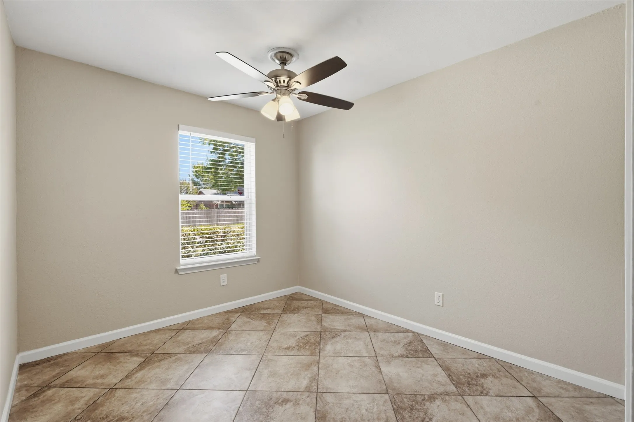 Travertine-look tile flooring, single window with blinds, ceiling fan with integrated lighting, and neutral wall tones