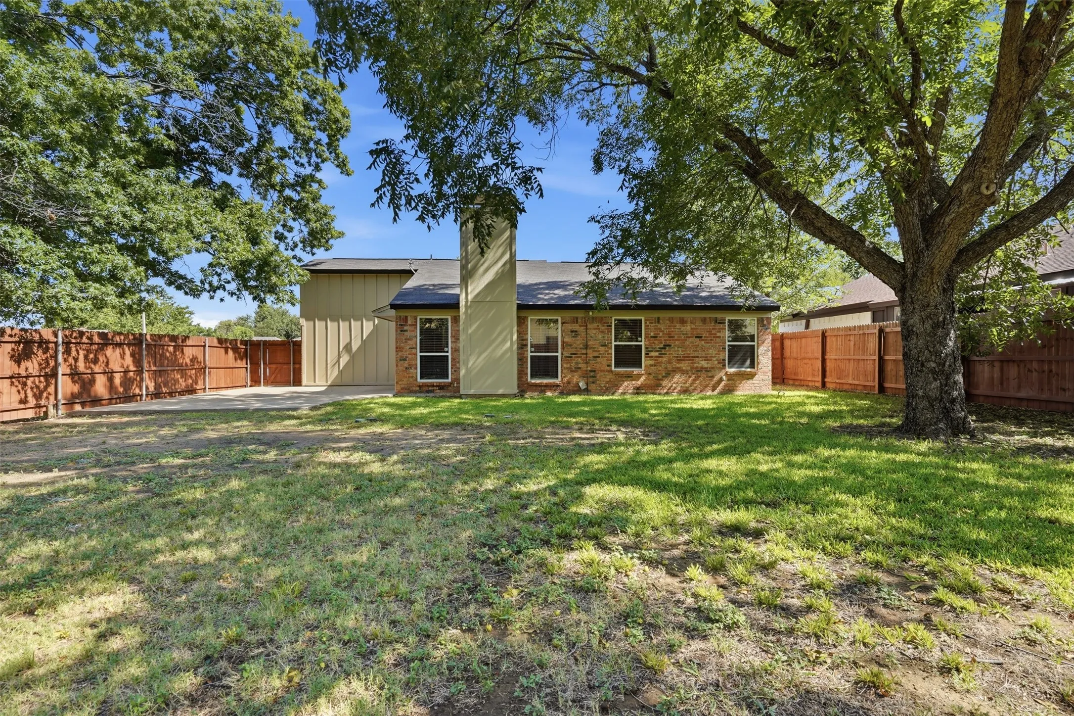Expansive backyard featuring a mature tree, privacy fencing, and a concrete patio