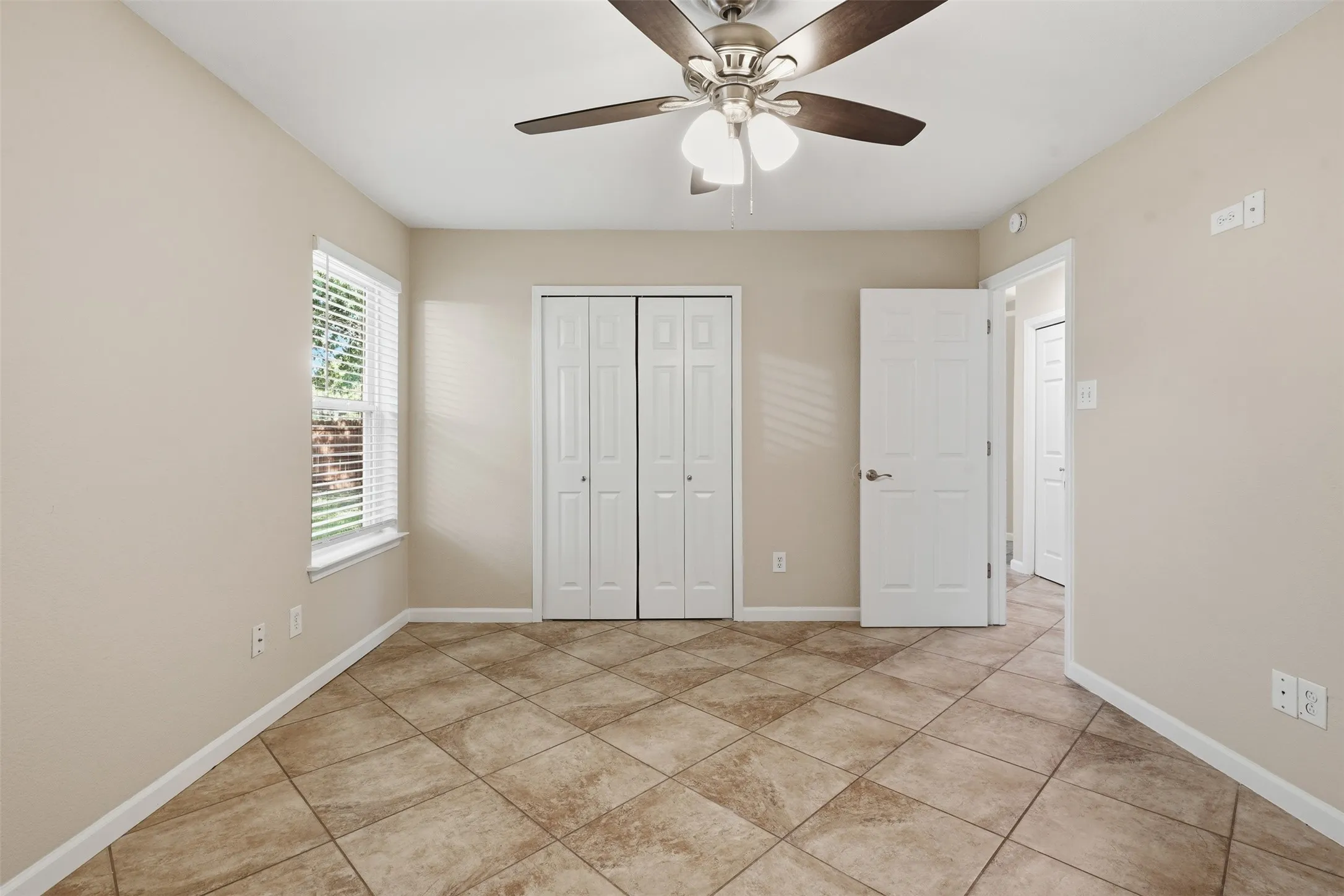 Neutral tone walls, ceiling fan with integrated lighting, window with blinds, bi-fold closet doors, and diagonal tile flooring