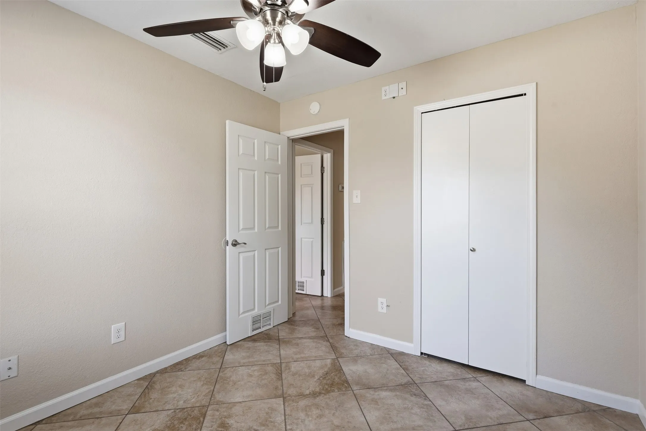 Neutral tone wall paint, tile flooring, ceiling fan with light fixture, white bi-fold closet doors, and a paneled interior door