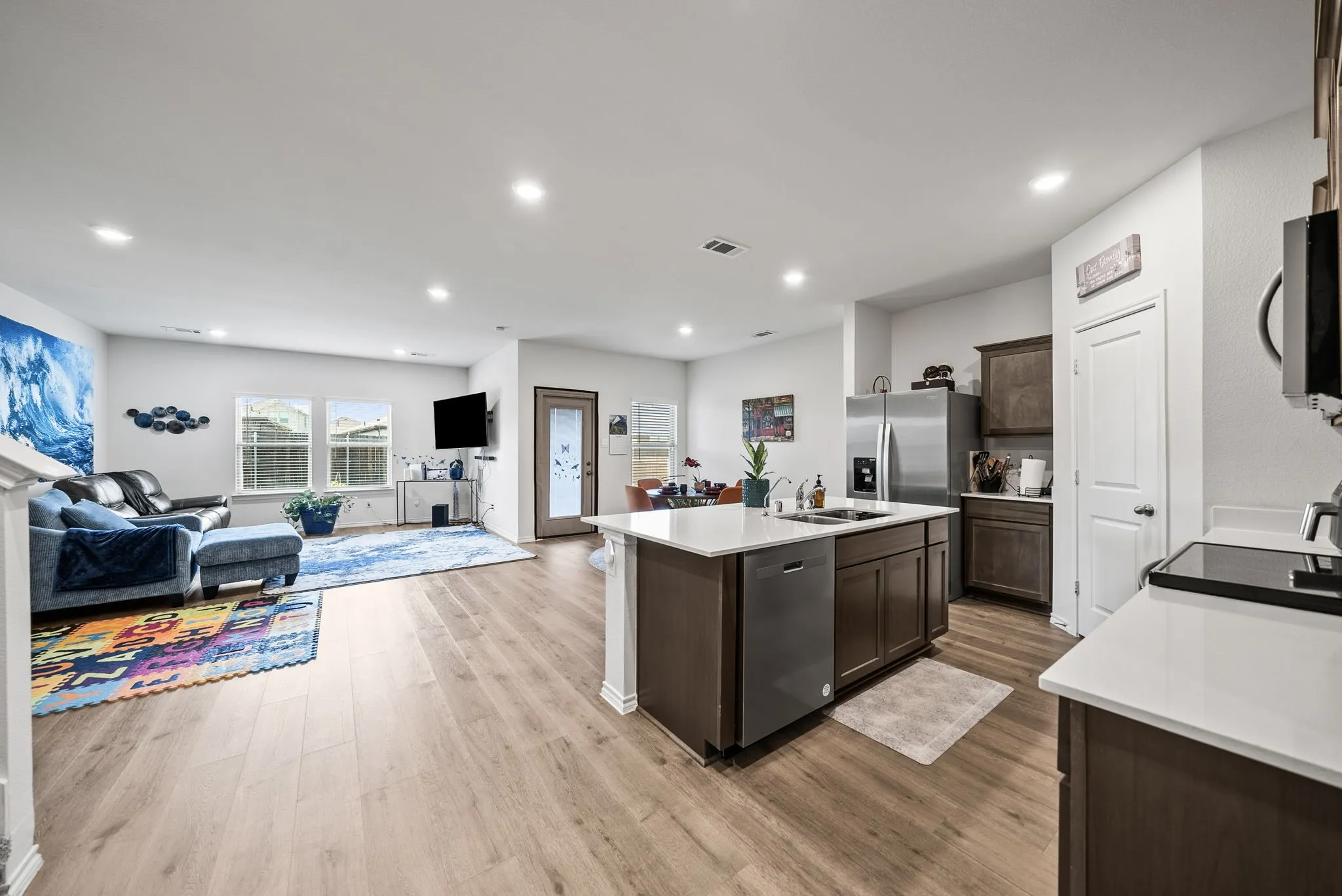 Open-concept living space featuring wood-finish flooring, recessed lighting, kitchen island with sink and integrated dishwasher, and stainless steel appliances