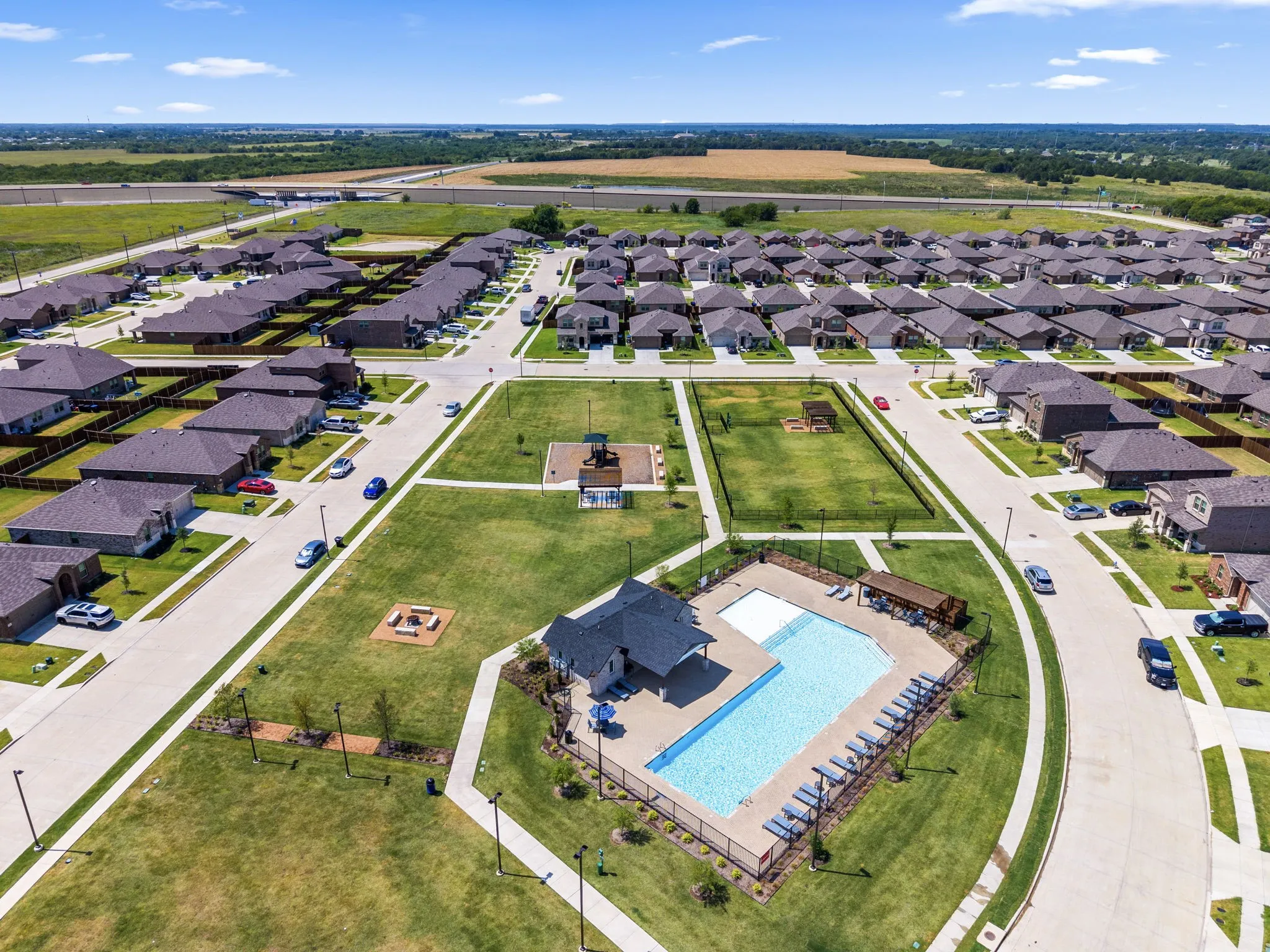 Aerial view of a well-planned residential community featuring a resort-style amenity center with an in-ground swimming pool, lounge seating areas, and manicured landscaping