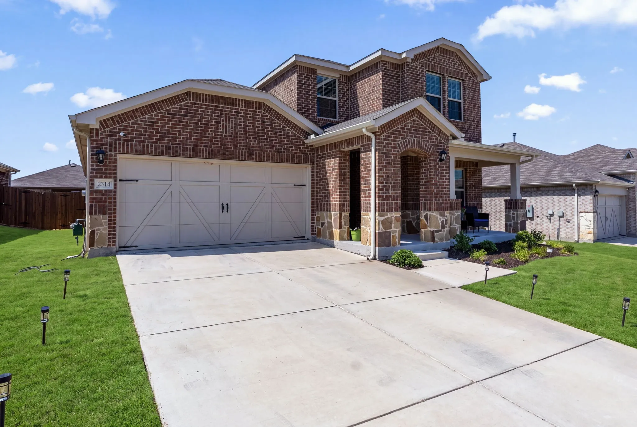 Brick two-story home featuring a two-car garage with carriage-style doors, concrete driveway, and manicured front lawn with professional landscaping