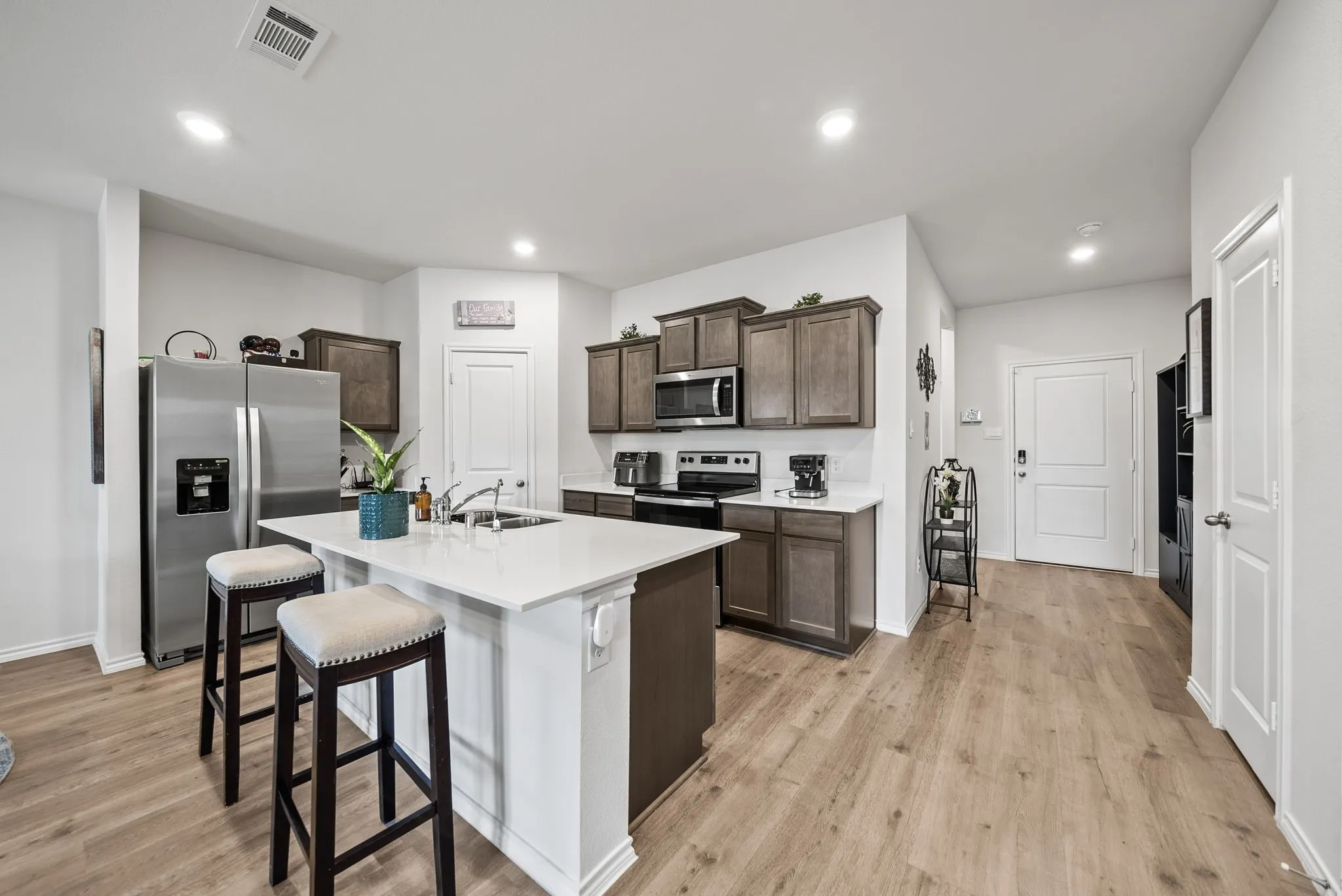 Modern kitchen featuring a large center island with white quartz countertop and seating for two, stainless steel appliances, wood-finish cabinetry with dark stain, wood-finish flooring throughout, and recessed lighting