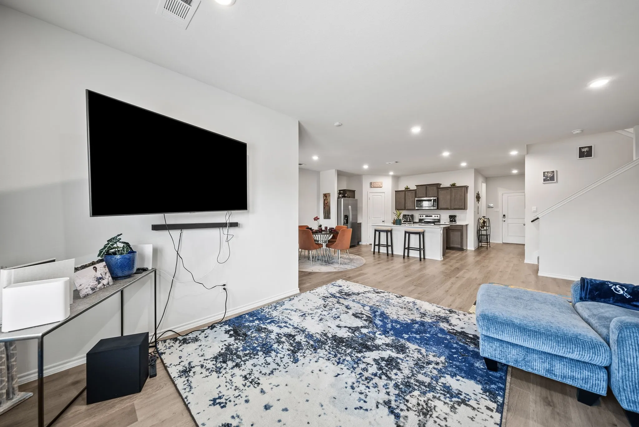 Open-concept layout featuring wood-finish flooring, recessed lighting, and a kitchen with an island, dark cabinetry, and stainless steel appliances