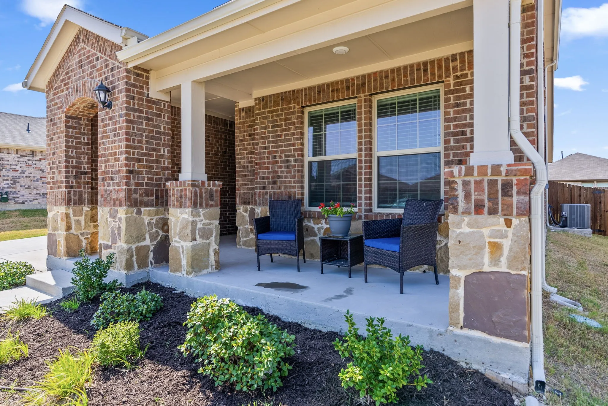 Covered front porch featuring substantial white columns, brick exterior with mixed-tone detailing, and large glass French doors opening to a concrete patio