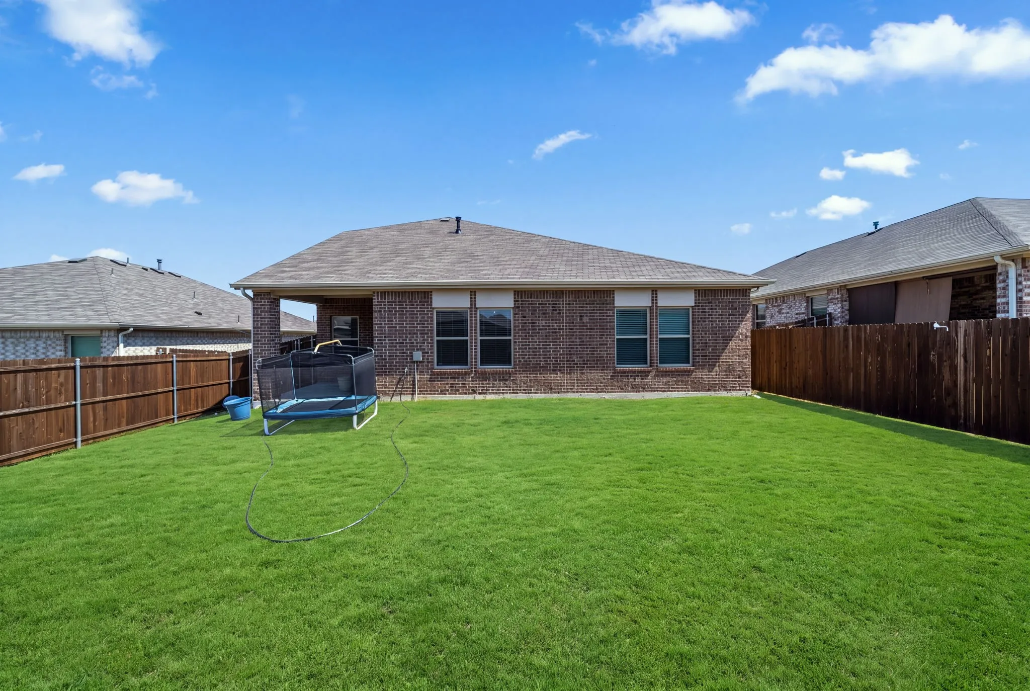 Expansive green lawn with a privacy fence and a brick-clad exterior