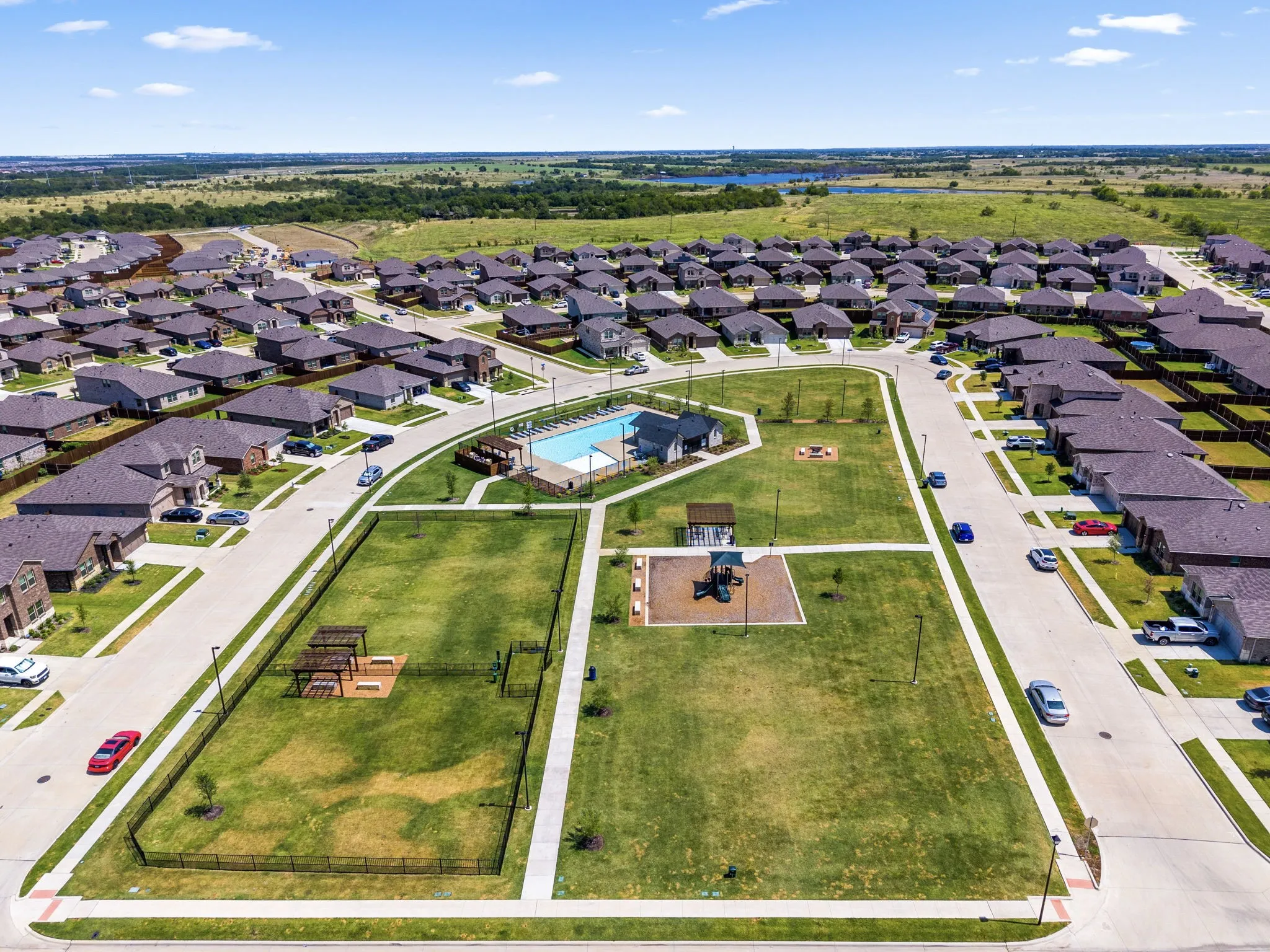 Community amenities courtyard featuring a resort-style swimming pool, manicured lawn spaces, playground area with equipment, and paved walkways throughout the gated recreational grounds, surrounded by newly constructed residential homes