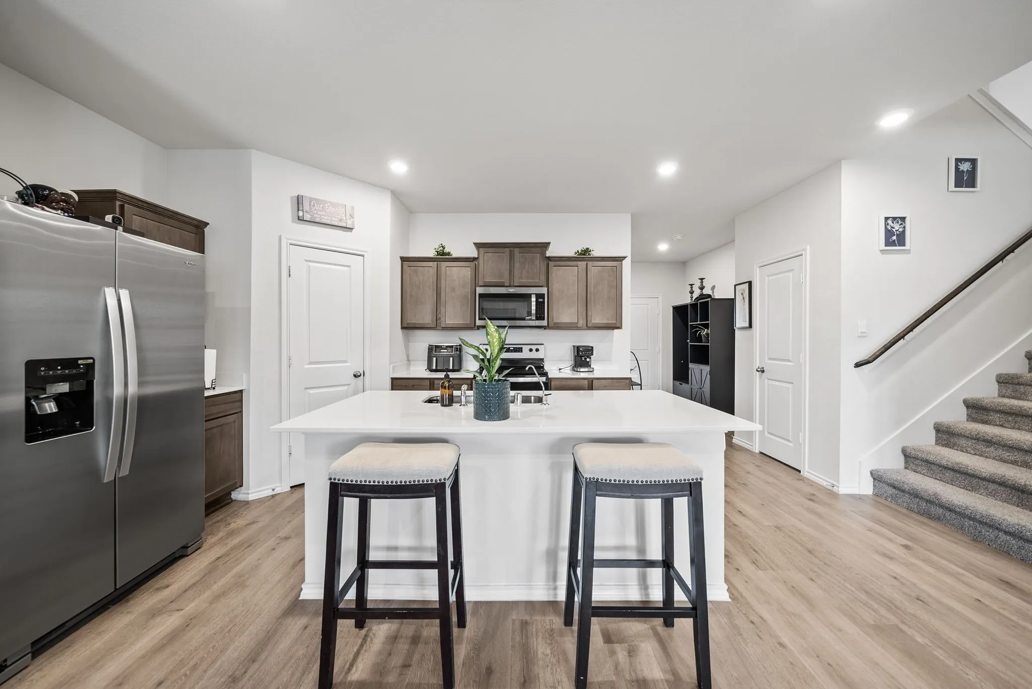 Modern kitchen featuring a large center island with waterfall countertop, stainless steel refrigerator and built-in microwave, wood-finish cabinetry, recessed lighting, and wood-finish flooring throughout