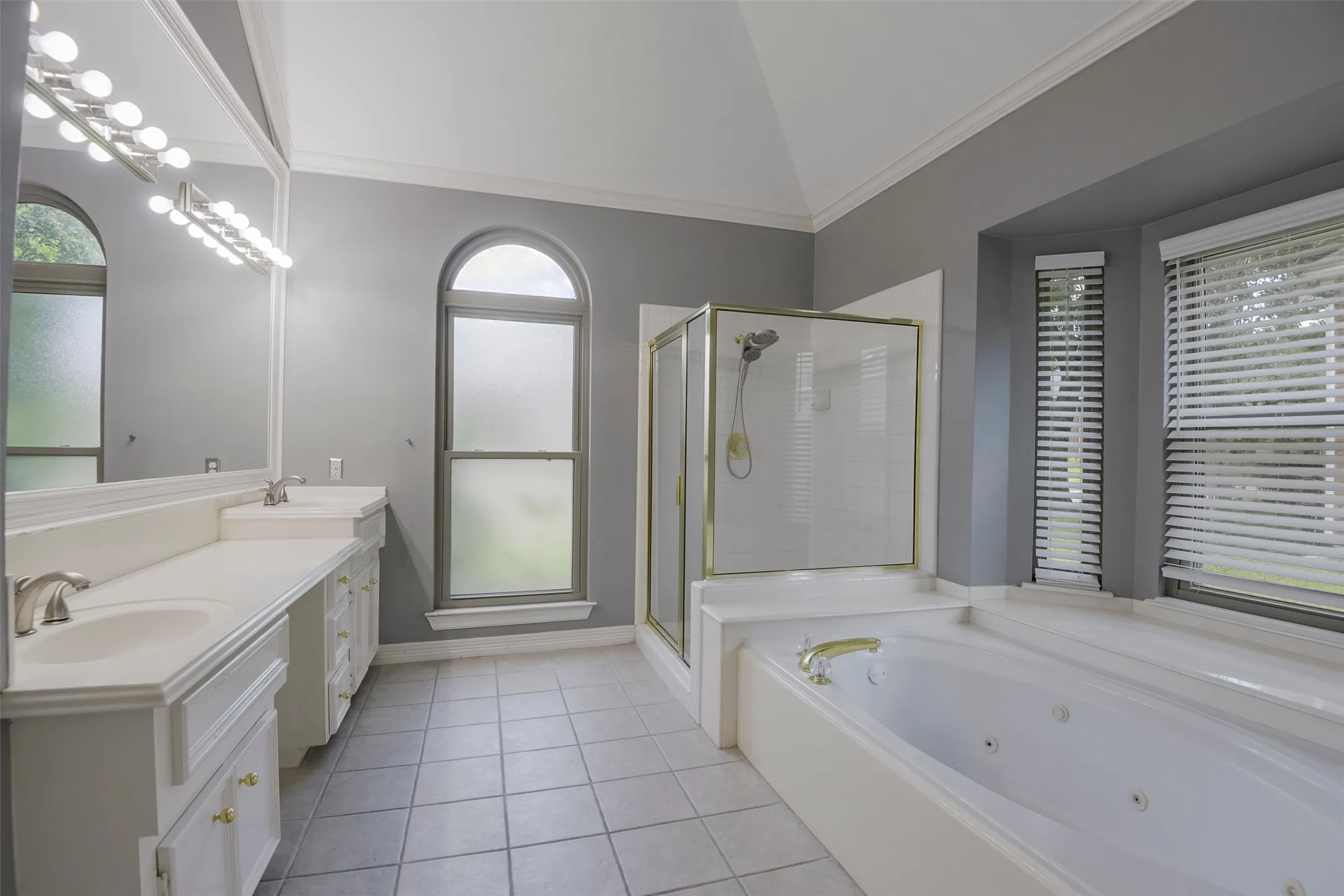 Vaulted ceiling, dual vanity, jetted soaking tub, glass-enclosed shower, and arched window