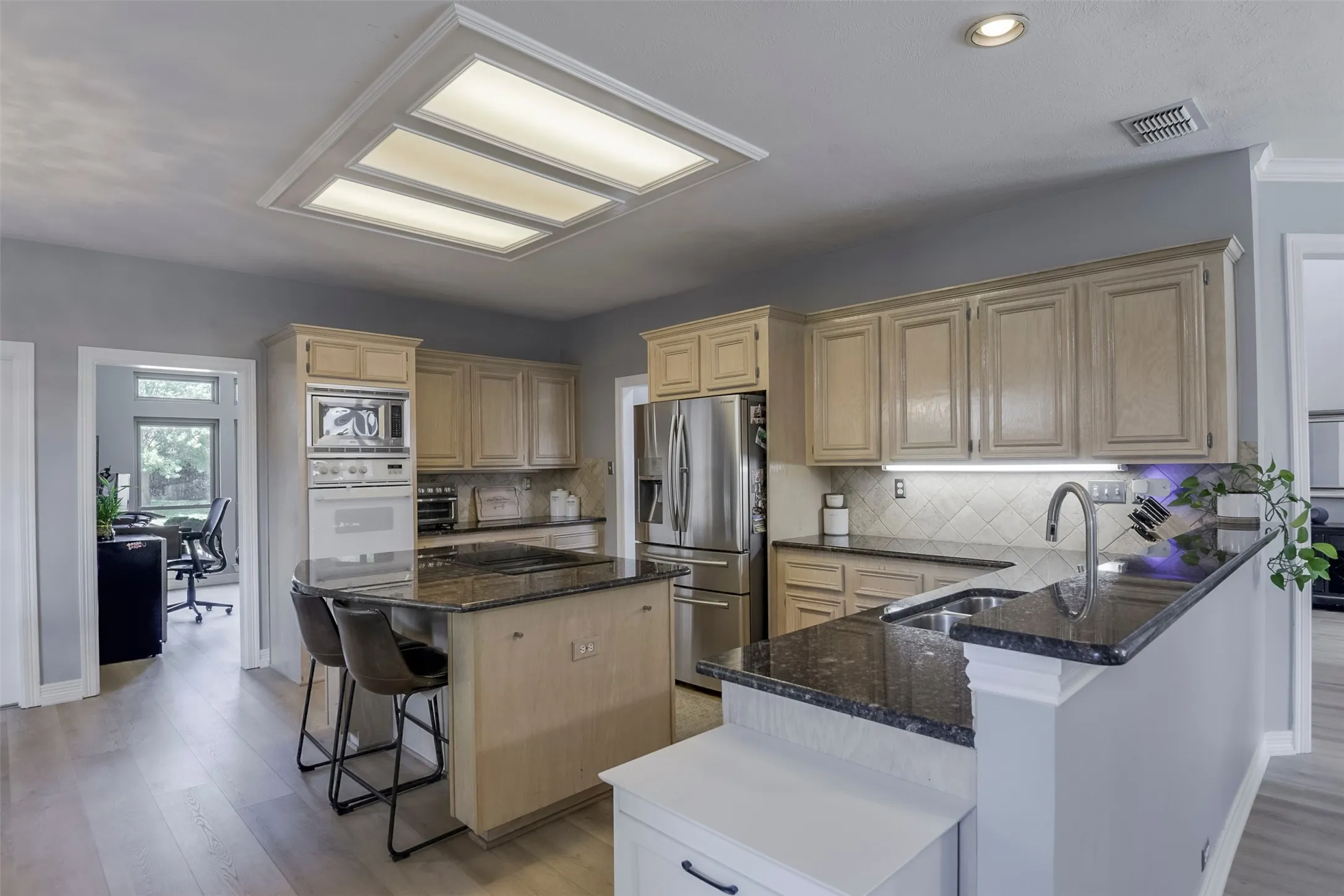 Kitchen with light wood-finish cabinetry, dark stone countertops, tile backsplash, stainless steel appliances, and a central island