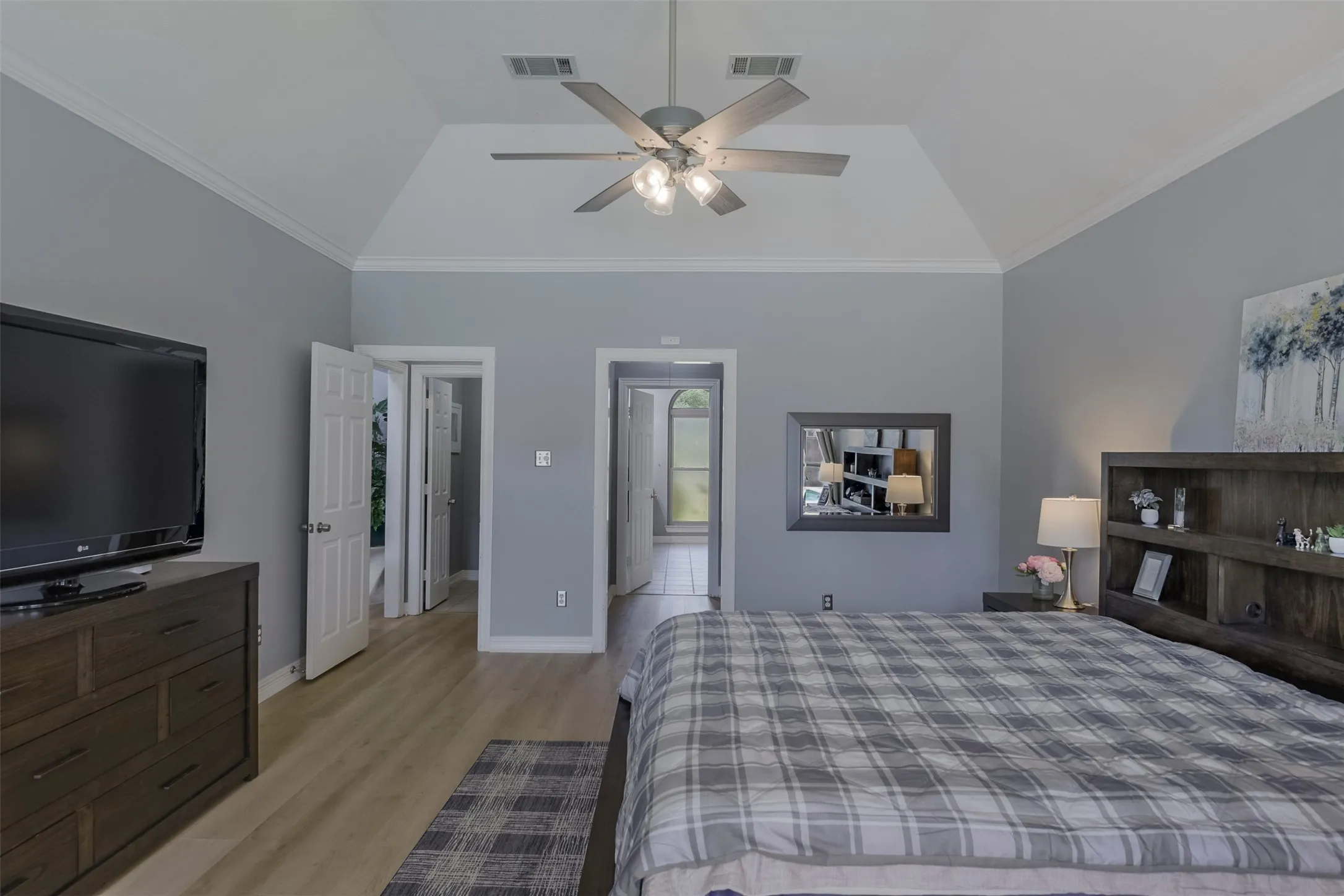 Vaulted ceiling with crown molding, wood-finish flooring, ceiling fan with integrated lighting, and multiple interior doorways