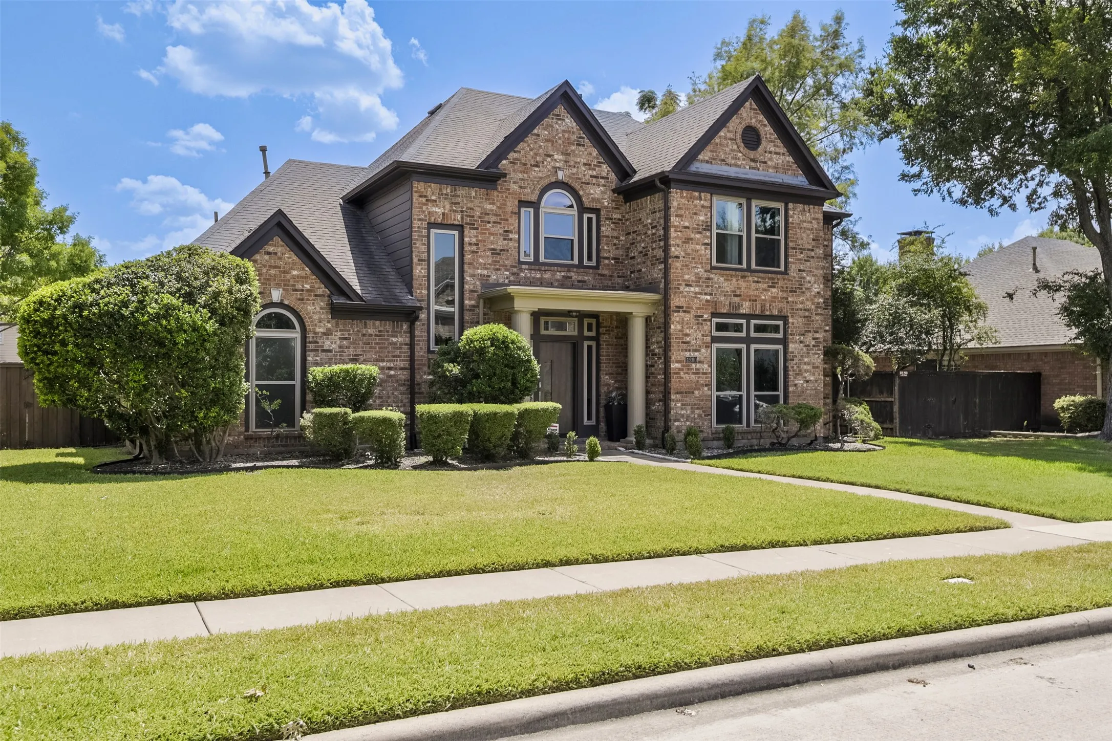 Brick and siding exterior with arched and rectangular windows, covered entry, and manicured landscaping