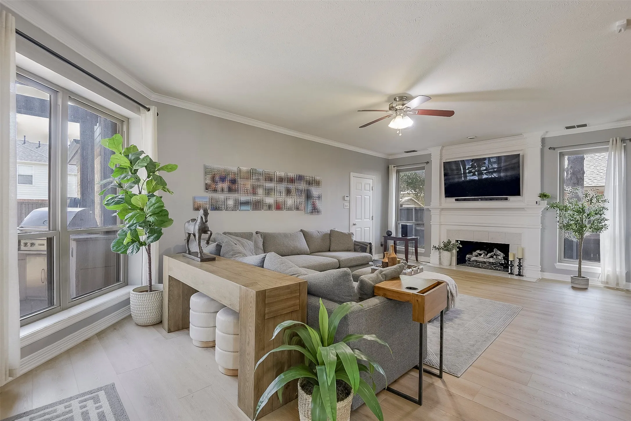 Living area featuring wood-finish flooring, a ceiling fan, and a fireplace with a stone mantel