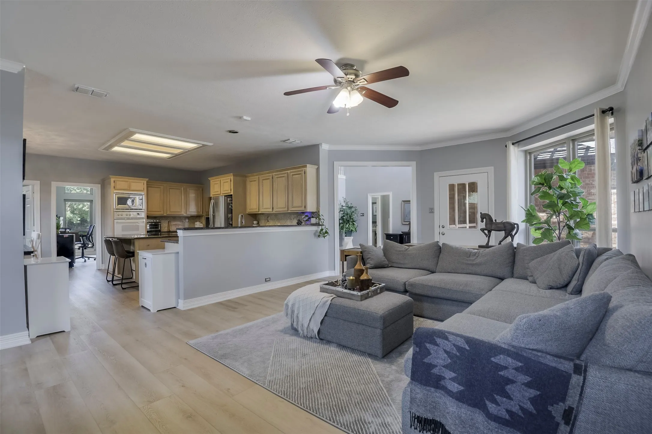 Expansive living area featuring wood-finish flooring, a ceiling fan, and crown molding